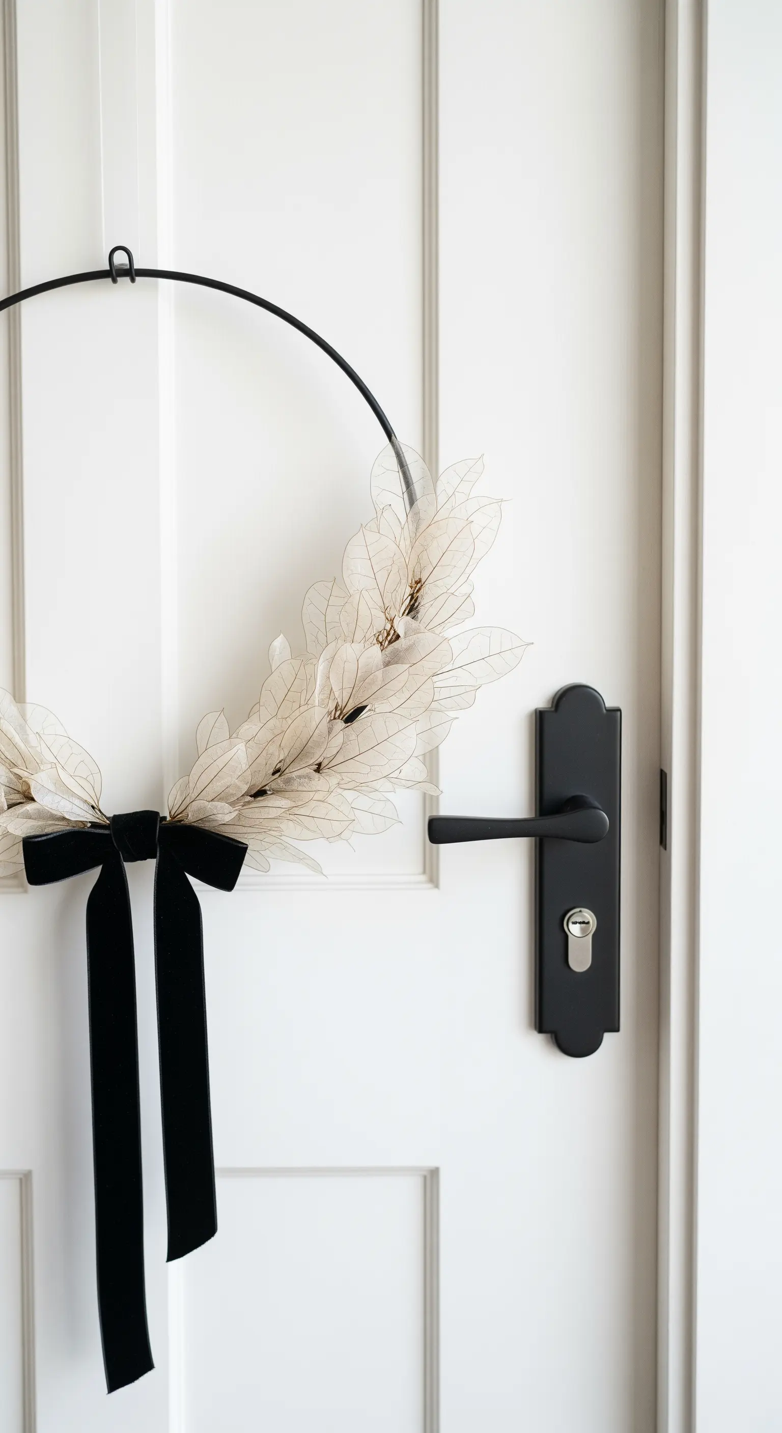 Weiße Tür mit asymmetrischem Kranz aus getrockneten hellen Blättern und schwarzem Band