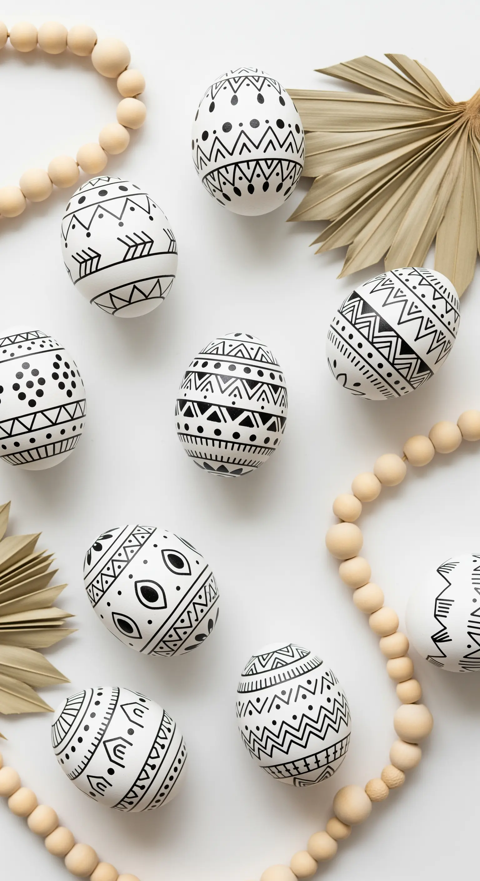 Schwarz-weiß gemusterte Eier mit Holzperlen und Palmblatt