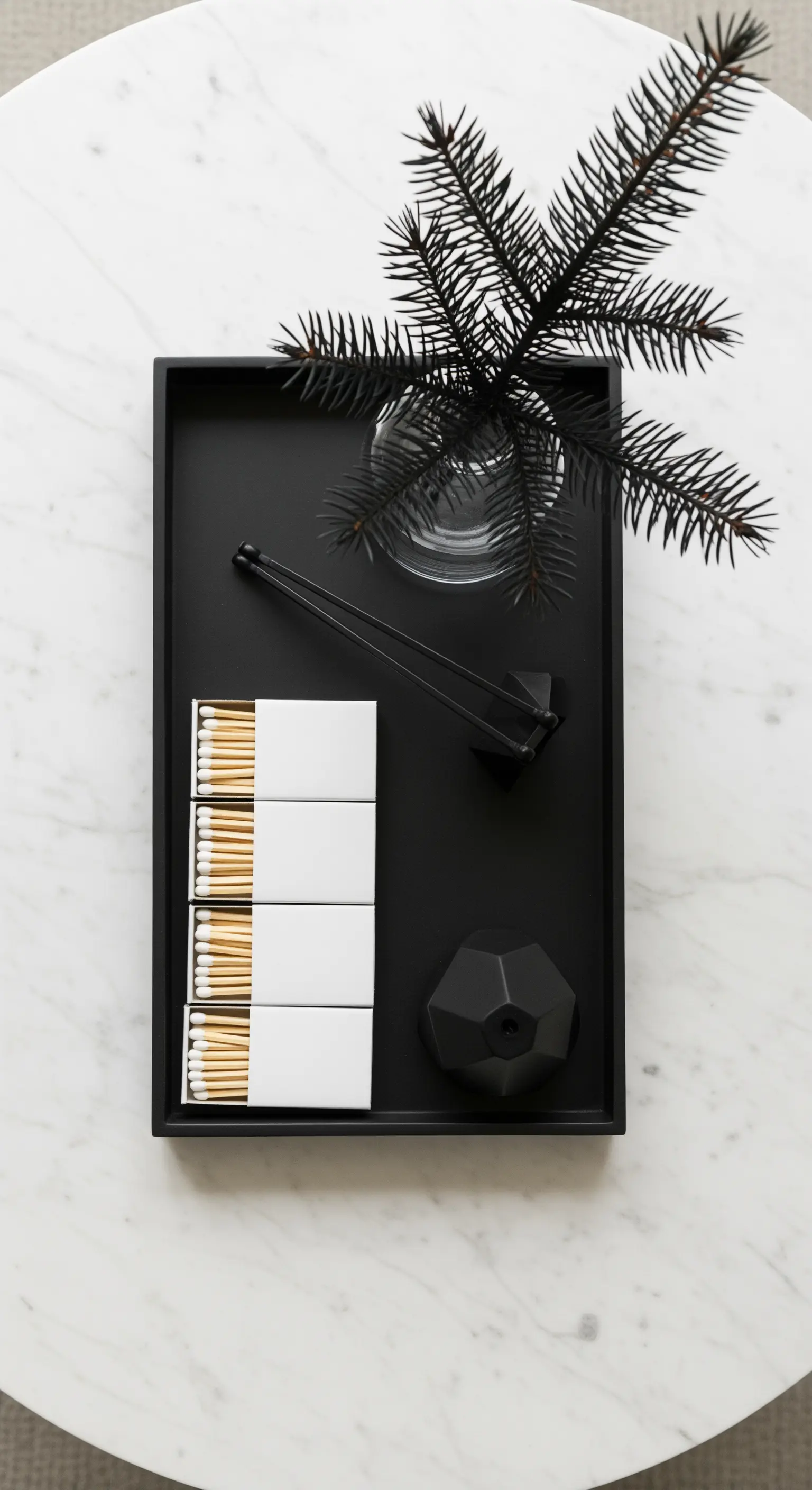 Schwarzes Tablett mit Streichhölzern, Kerzenlöscher und Tannenzweig auf Marmortisch