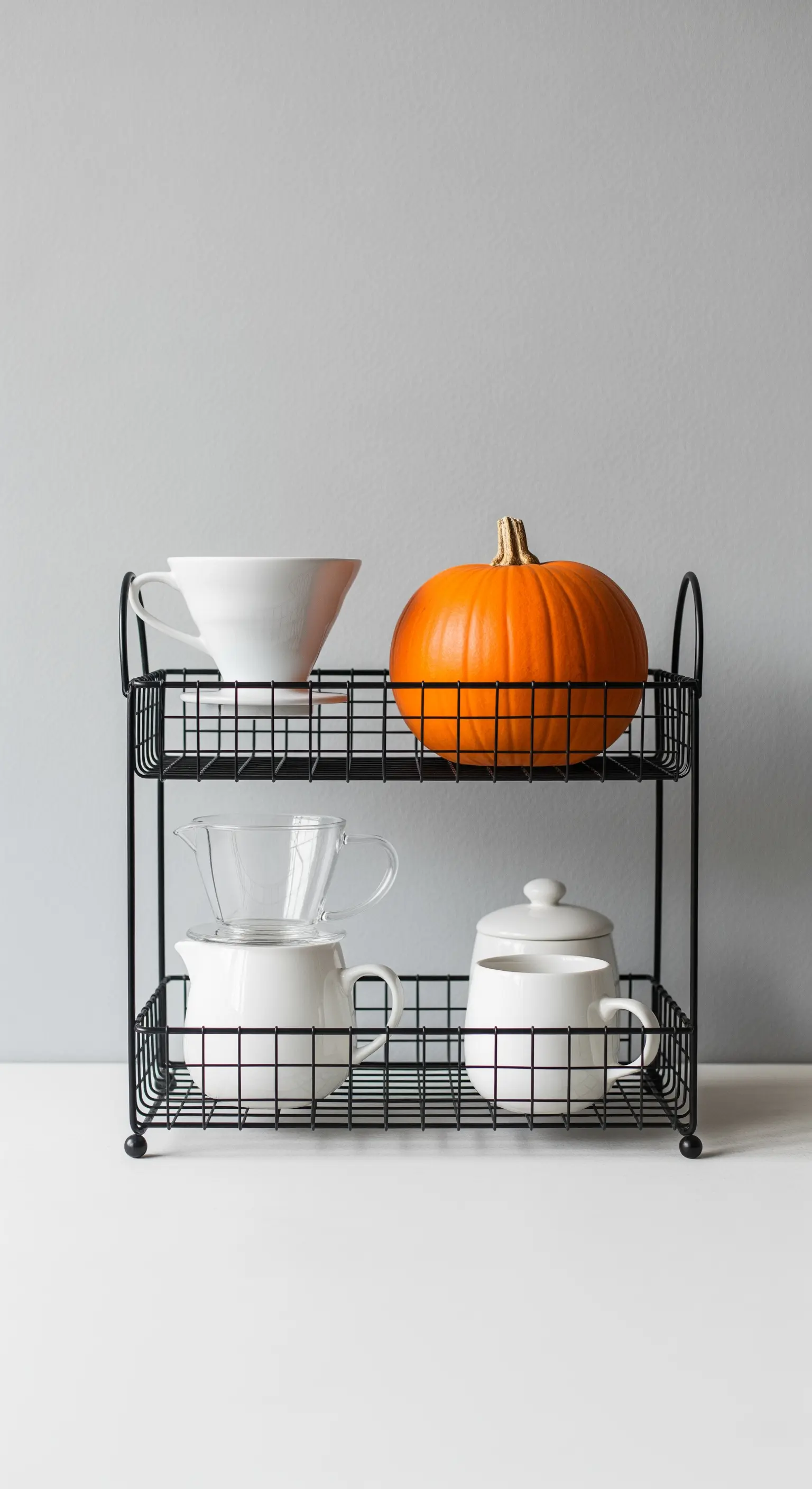 Schwarzes Drahtgestell mit weißem Kaffeezubehör und einem einzelnen orangen Kürbis