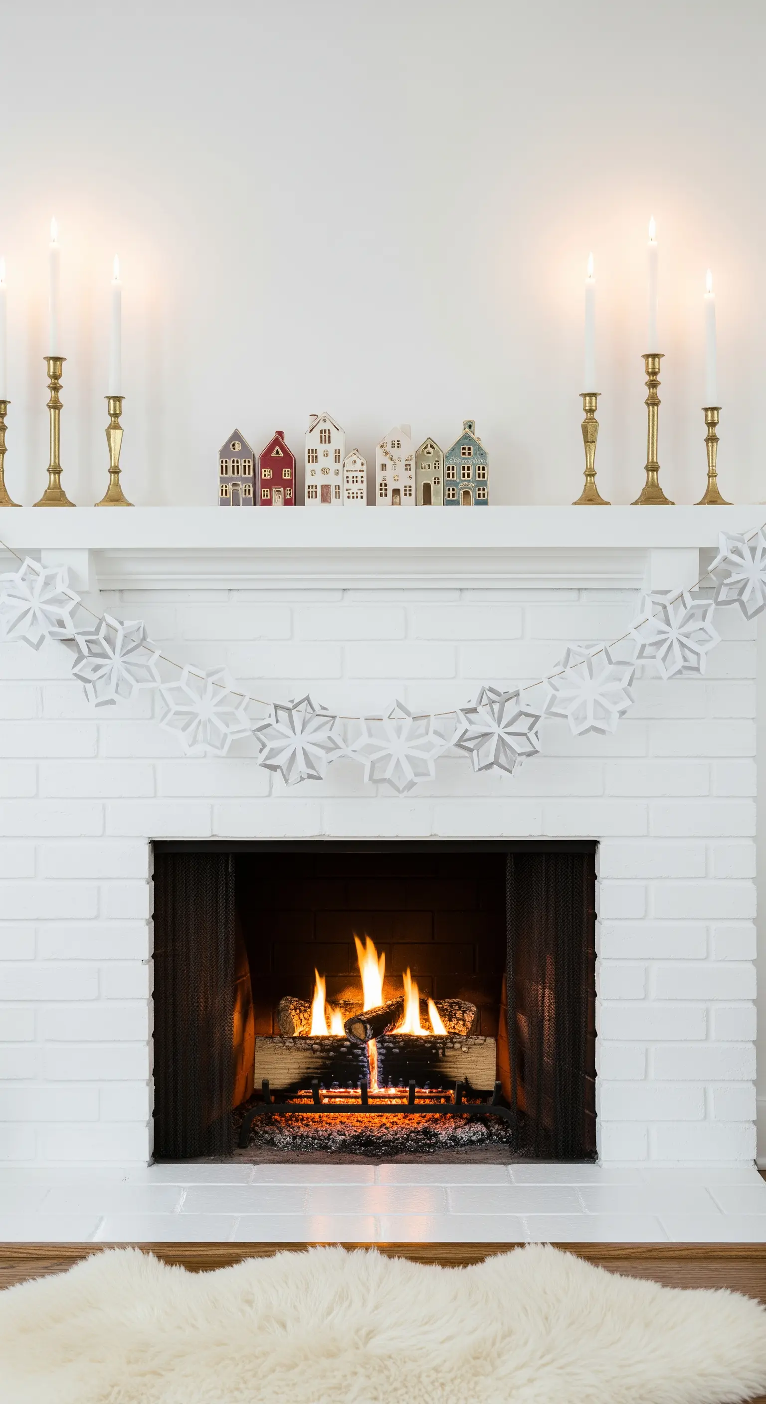 Weiße Papier-Schneeflocken-Girlande am weißen Kamin mit kleinen Keramikhäusern.