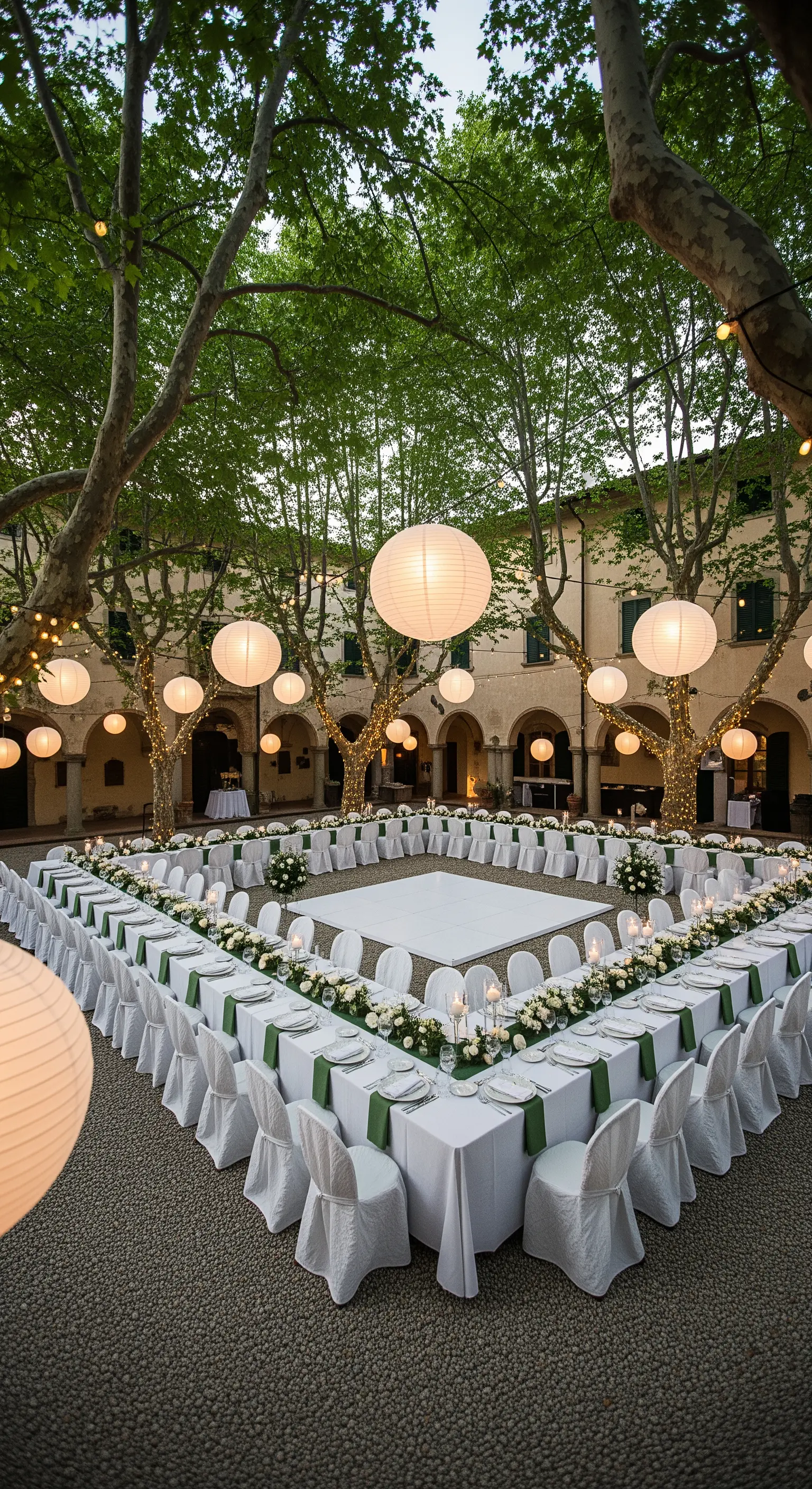 Quadratische Tischanordnung in einem Innenhof um eine weiße Tanzfläche mit Lampions