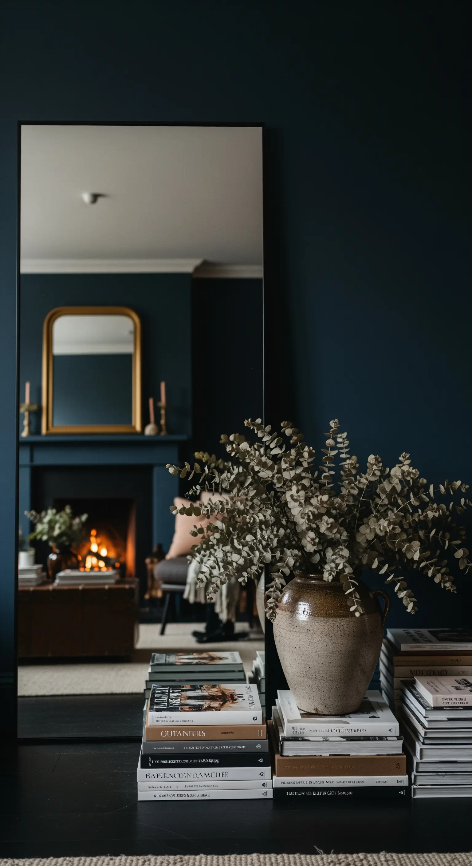 Große Vase mit Eukalyptus auf Büchern vor dunklem Kamin