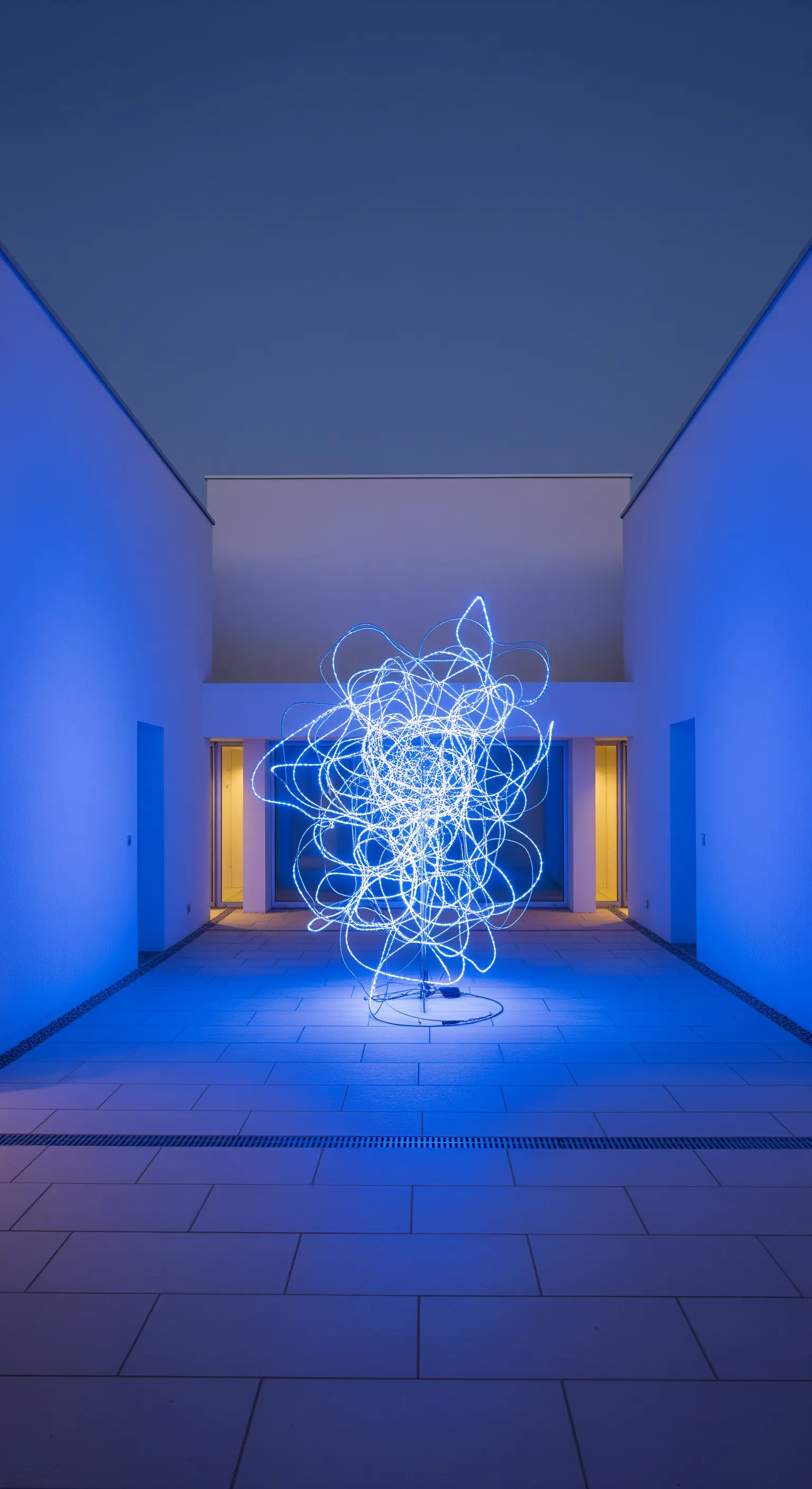 Abstrakte Lichtskulptur aus blauem Neonlicht in einem modernen, minimalistischen Innenhof.