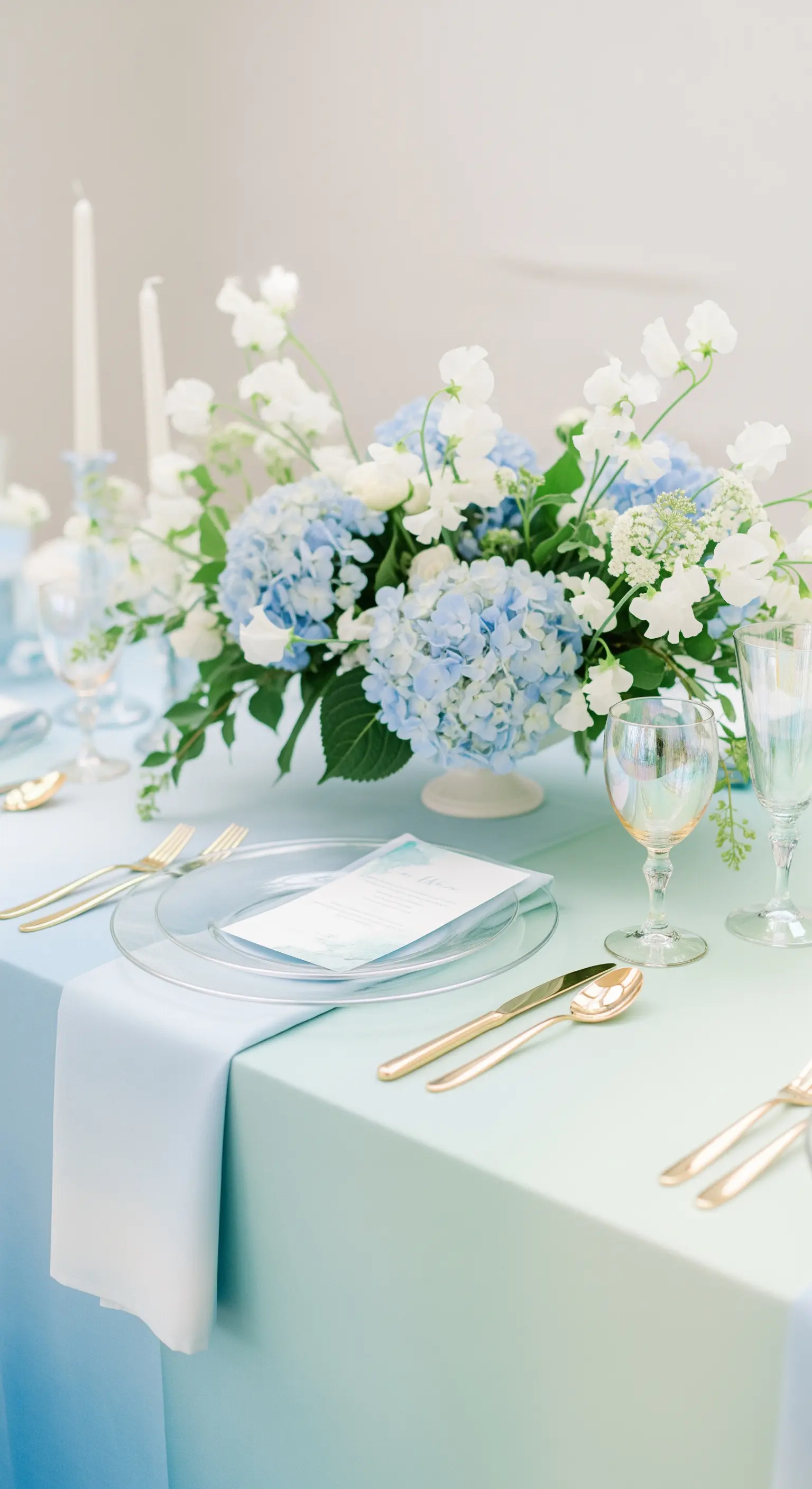 Zarte Tischdeko mit blauen Hortensien auf einem blau-grünen Ombré-Tischtuch