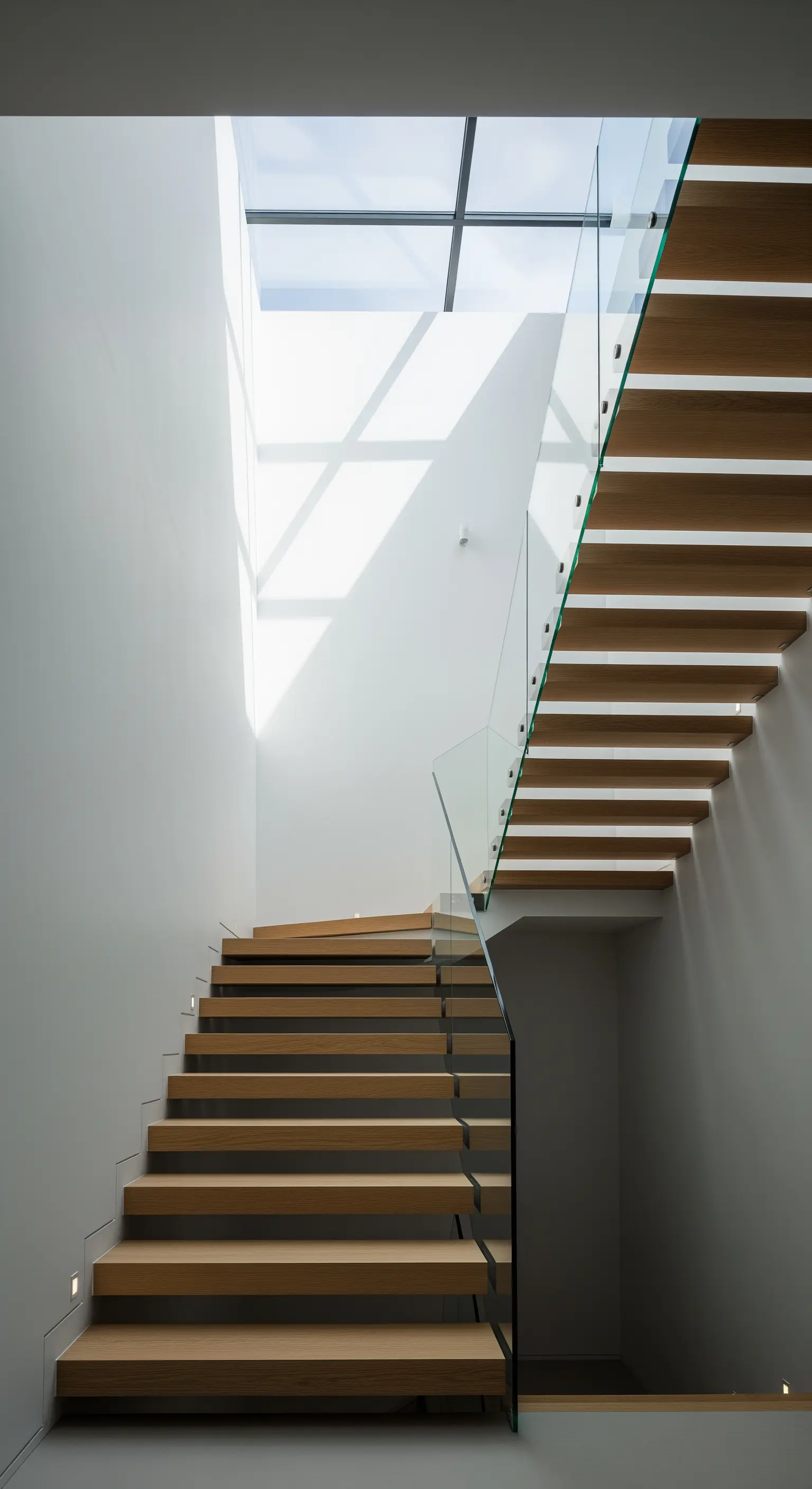 Eine moderne Holztreppe mit Glasgeländer, die durch Tageslicht von oben inszeniert wird.