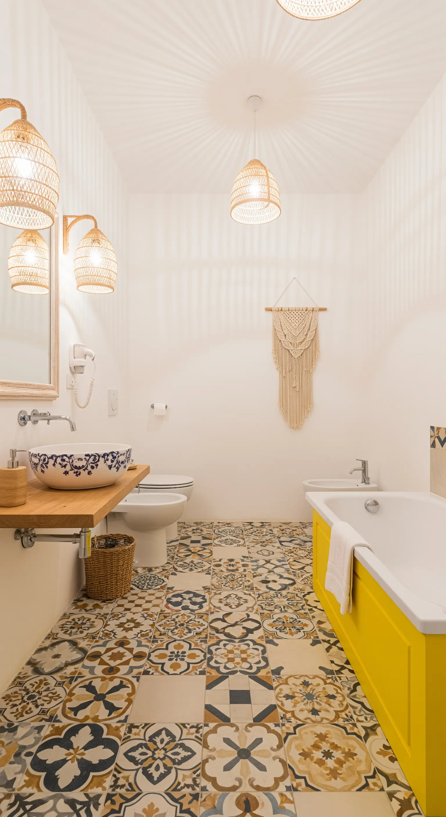 Helles Badezimmer mit gemusterten Bodenfliesen, Rattanlampen und einer gelben Badewanne.