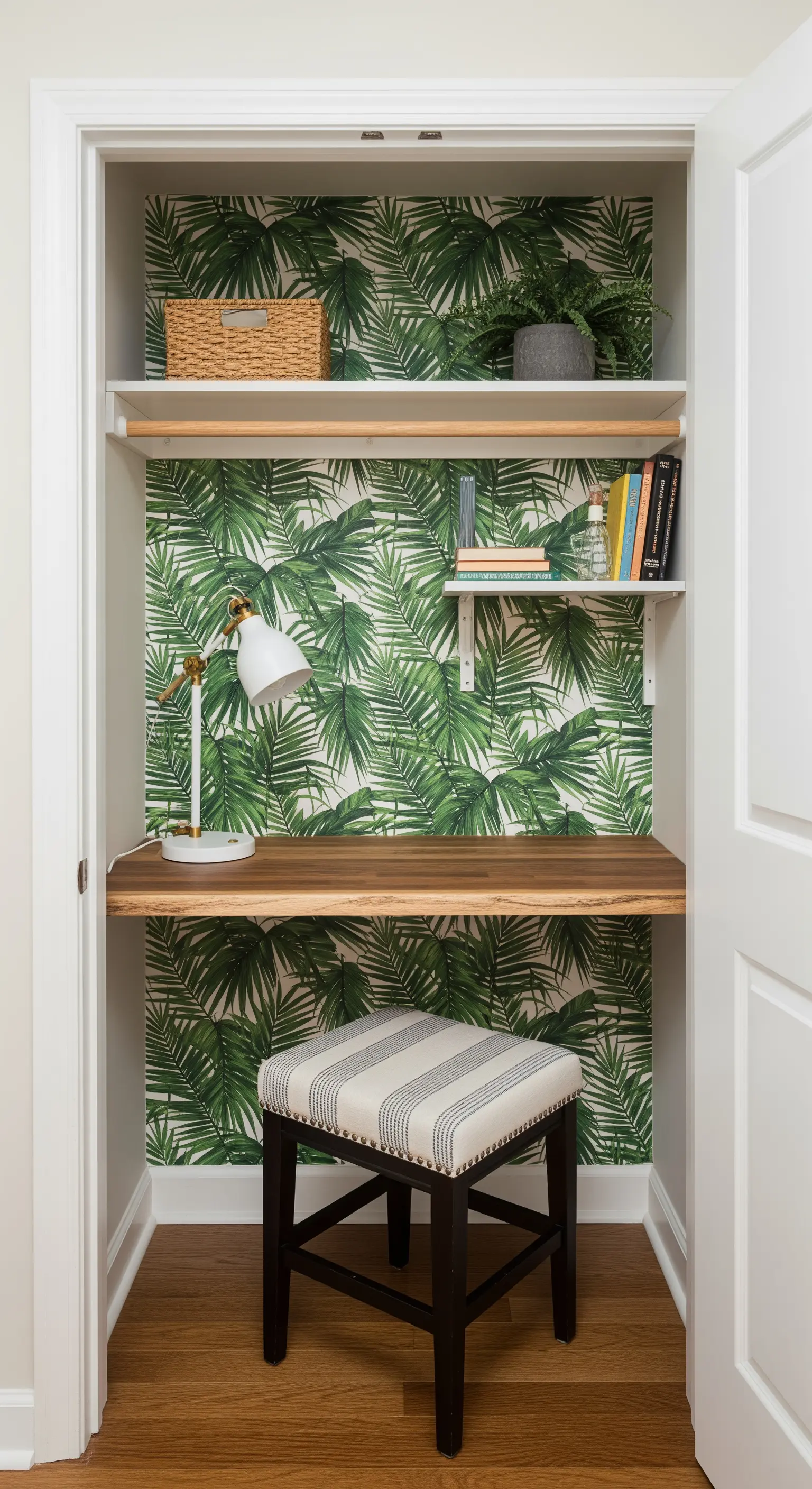 Ein kleiner Arbeitsplatz, der in einen Kleiderschrank mit tropischer Tapete integriert ist.
