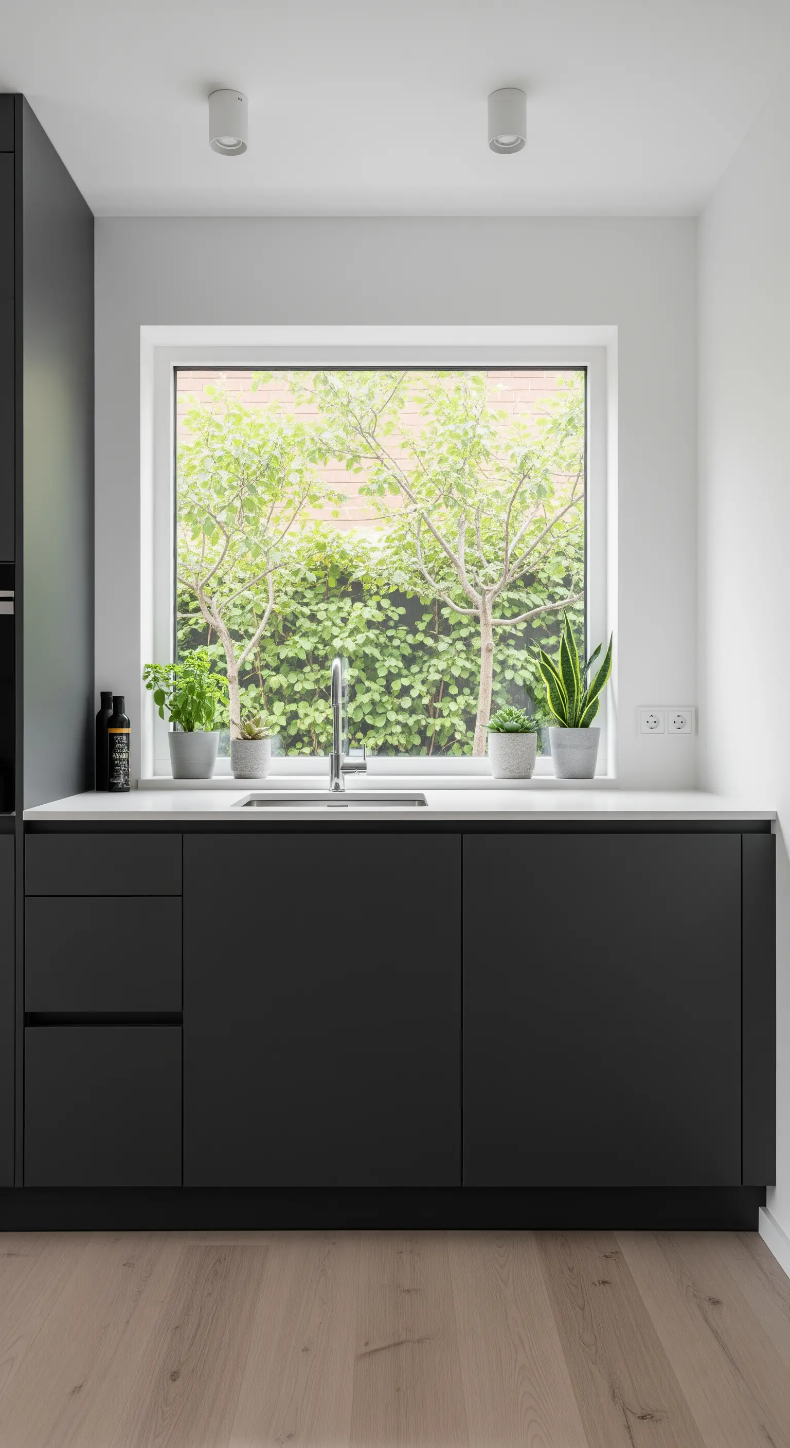 Moderne schwarze Küche mit großem Fenster, das den Blick auf grüne Pflanzen freigibt.