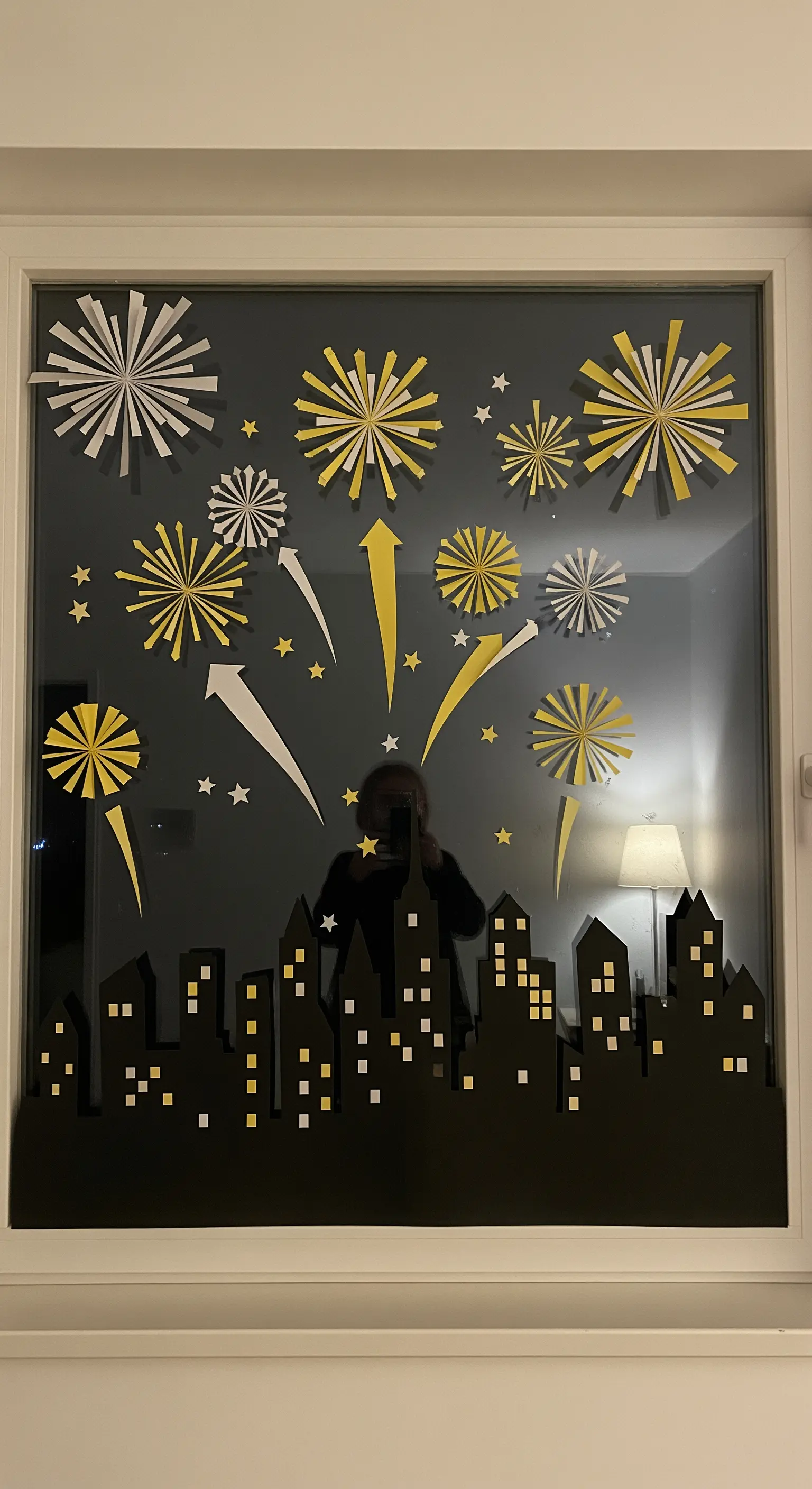 Eine Fensterscheibe, dekoriert mit einer Papiersilhouette einer Stadt und Feuerwerk.