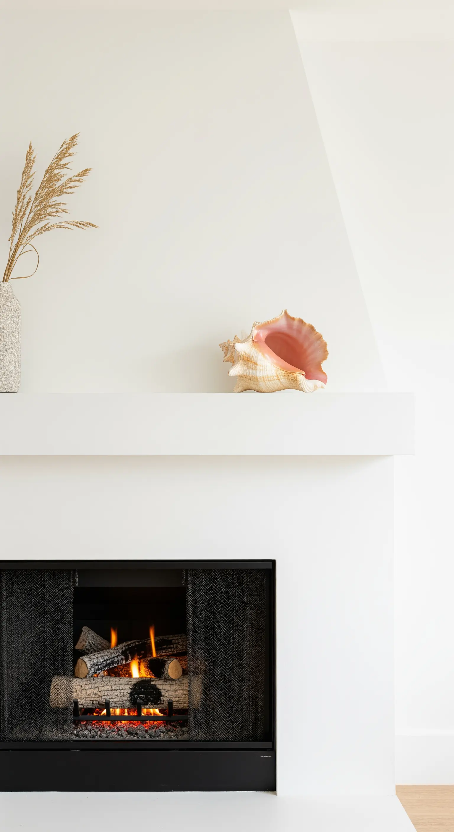 Minimalistischer weißer Kamin mit einer großen Muschel und Trockengras.