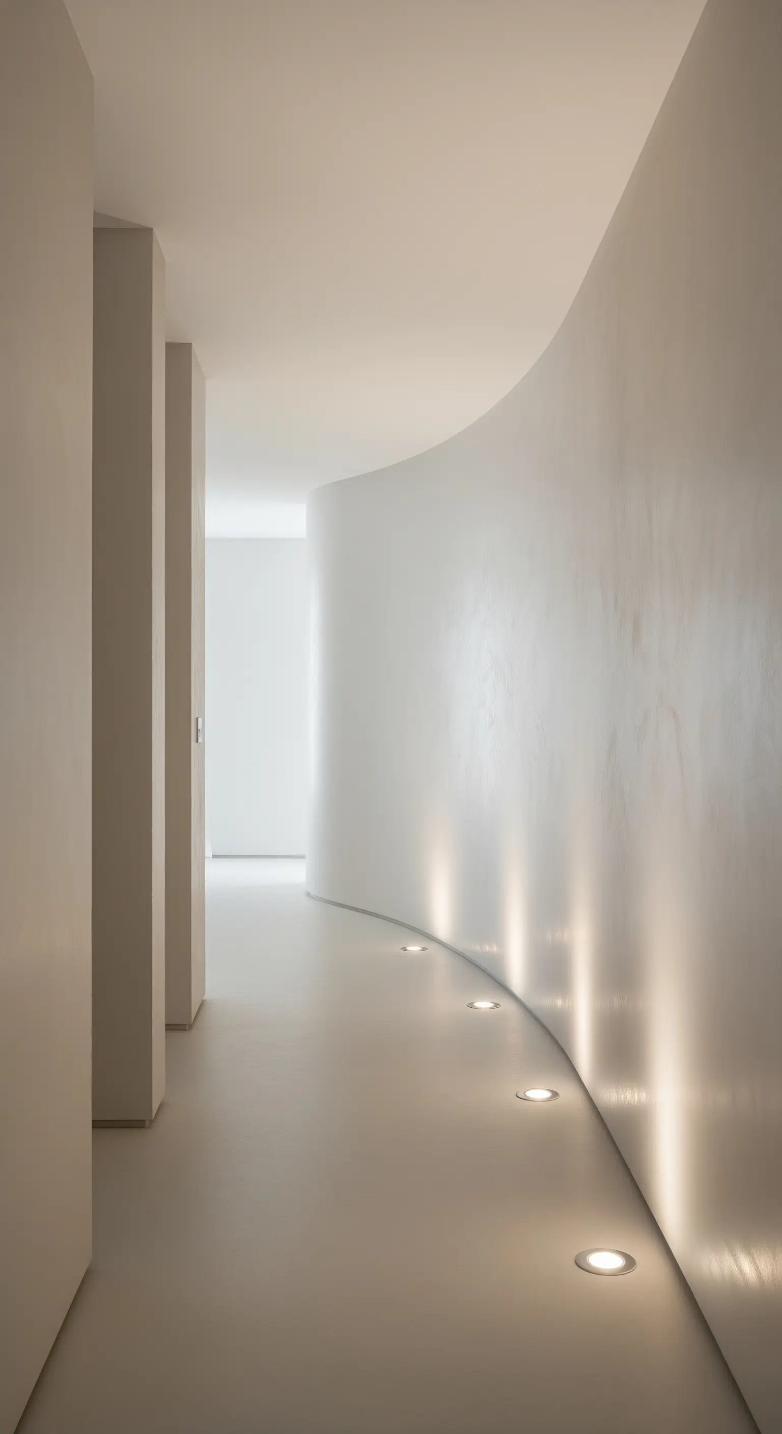 Geschwungene Wand in einem Flur, die von bodennahen Einbauspots beleuchtet wird.