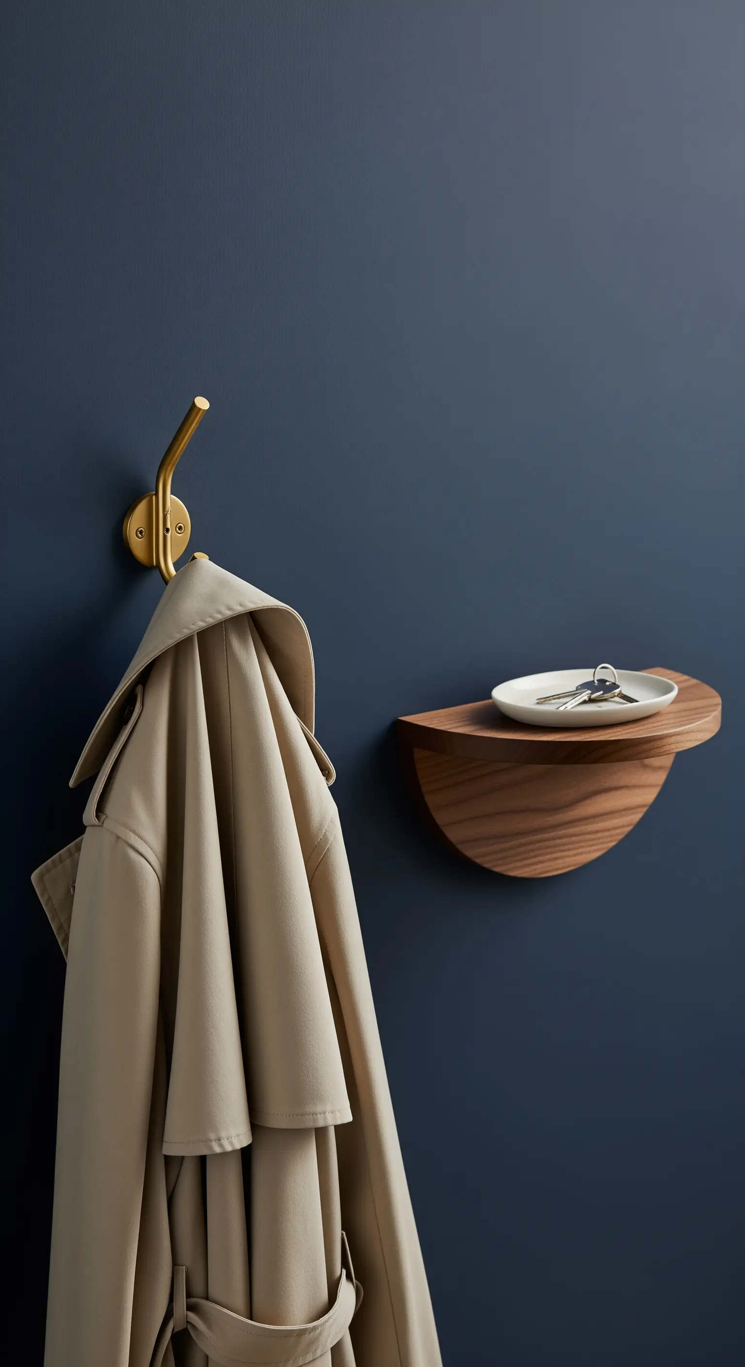 Eleganter Messinghaken und eine kleine Holzablage für Schlüssel an einer dunkelblauen Wand.