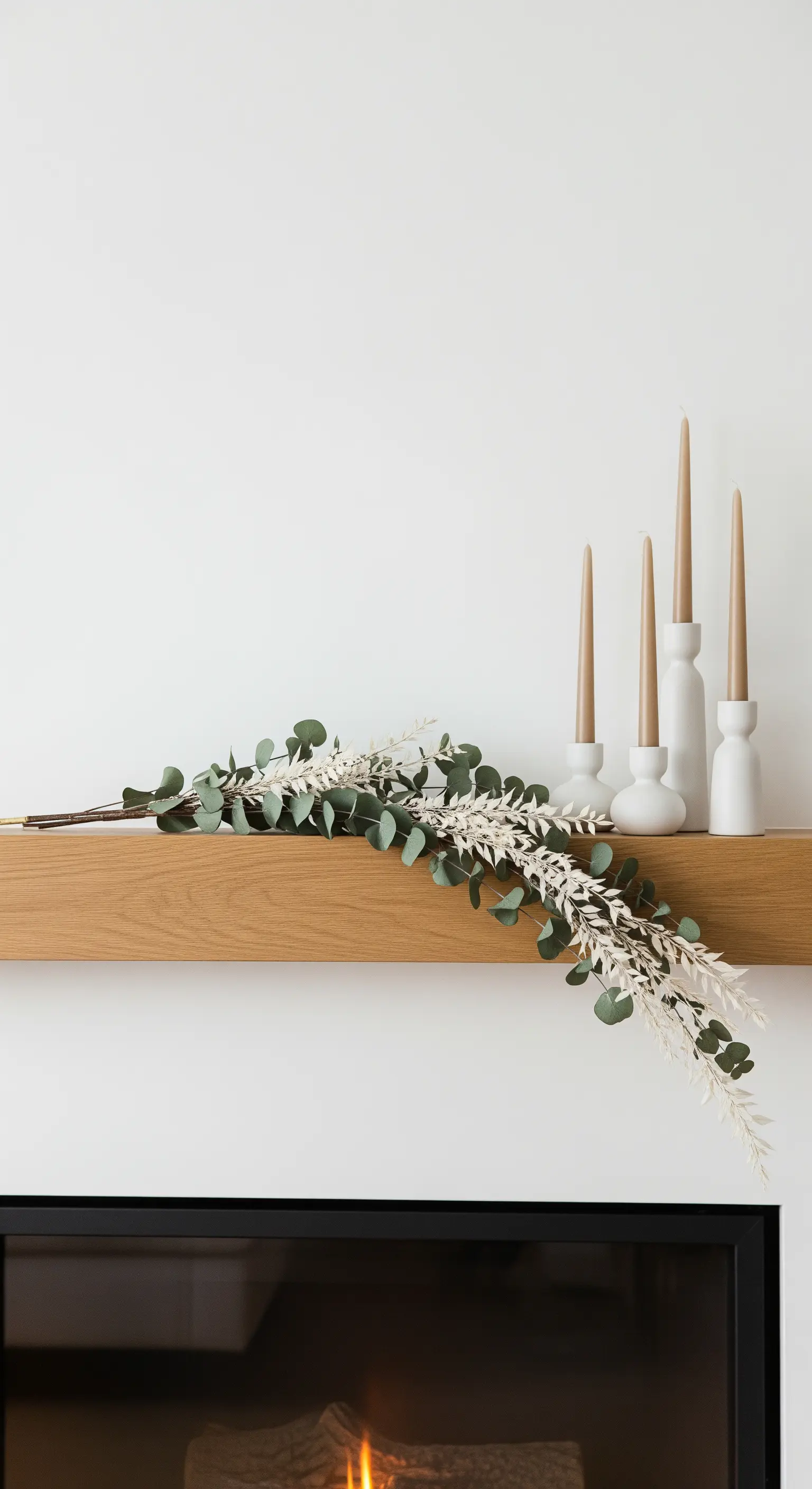 Minimalistische Dekoration auf einem Kaminsims aus Holz mit Kerzen und Eukalyptus.