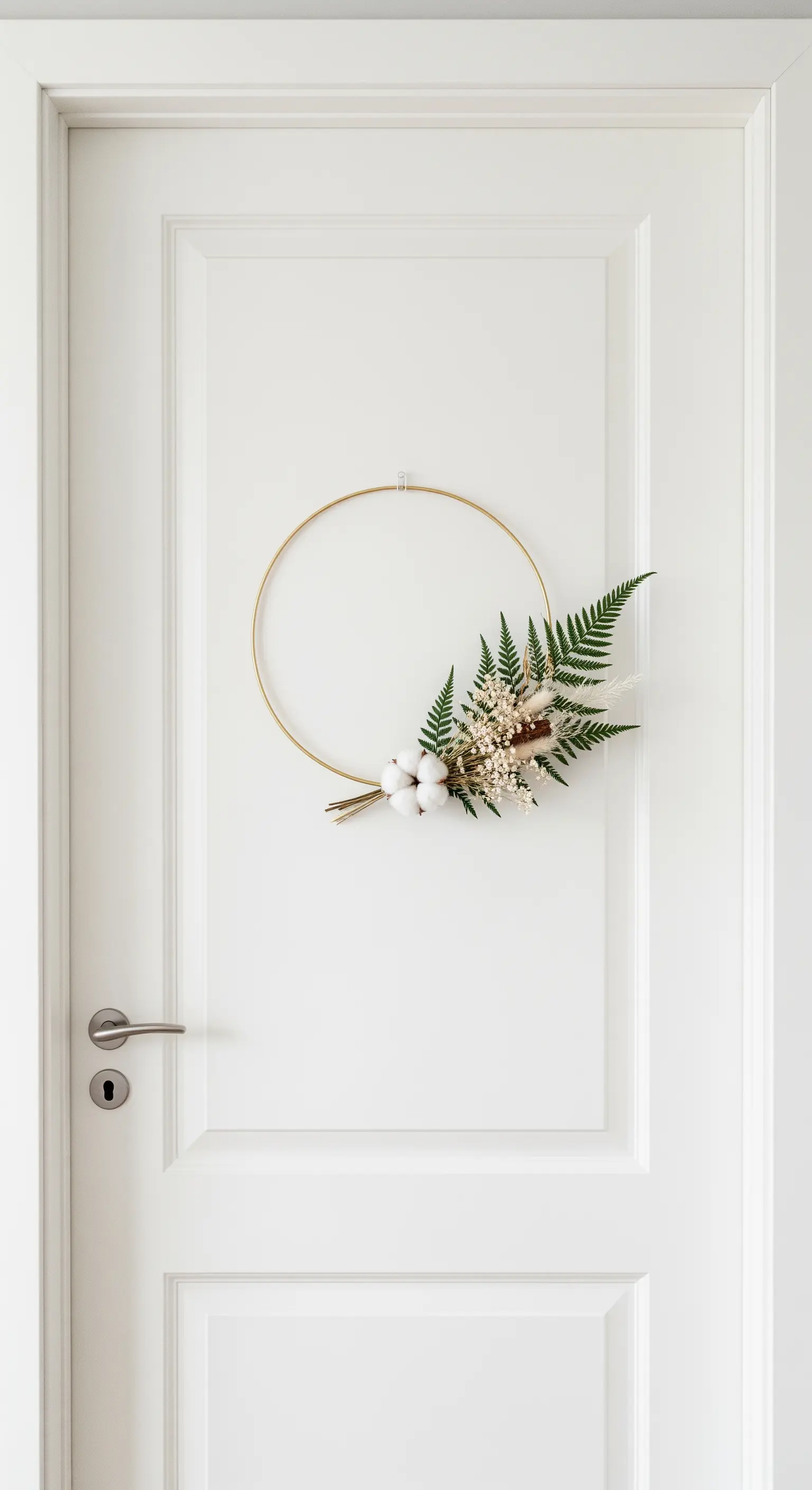 Moderner, minimalistischer Kranz an einer weißen Tür mit Trockenblumen auf einem goldenen Ring.