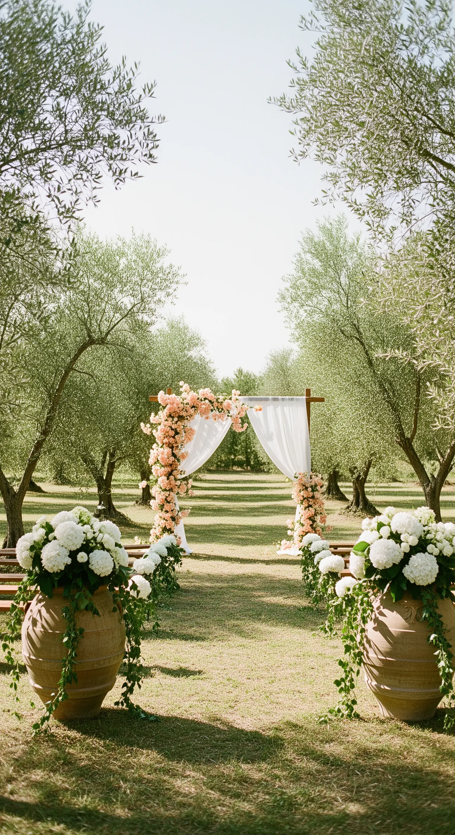 Hochzeitsbogen mit pfirsichfarbenen Rosen und weißem Stoff, flankiert von großen Terrakotta-Töpfen