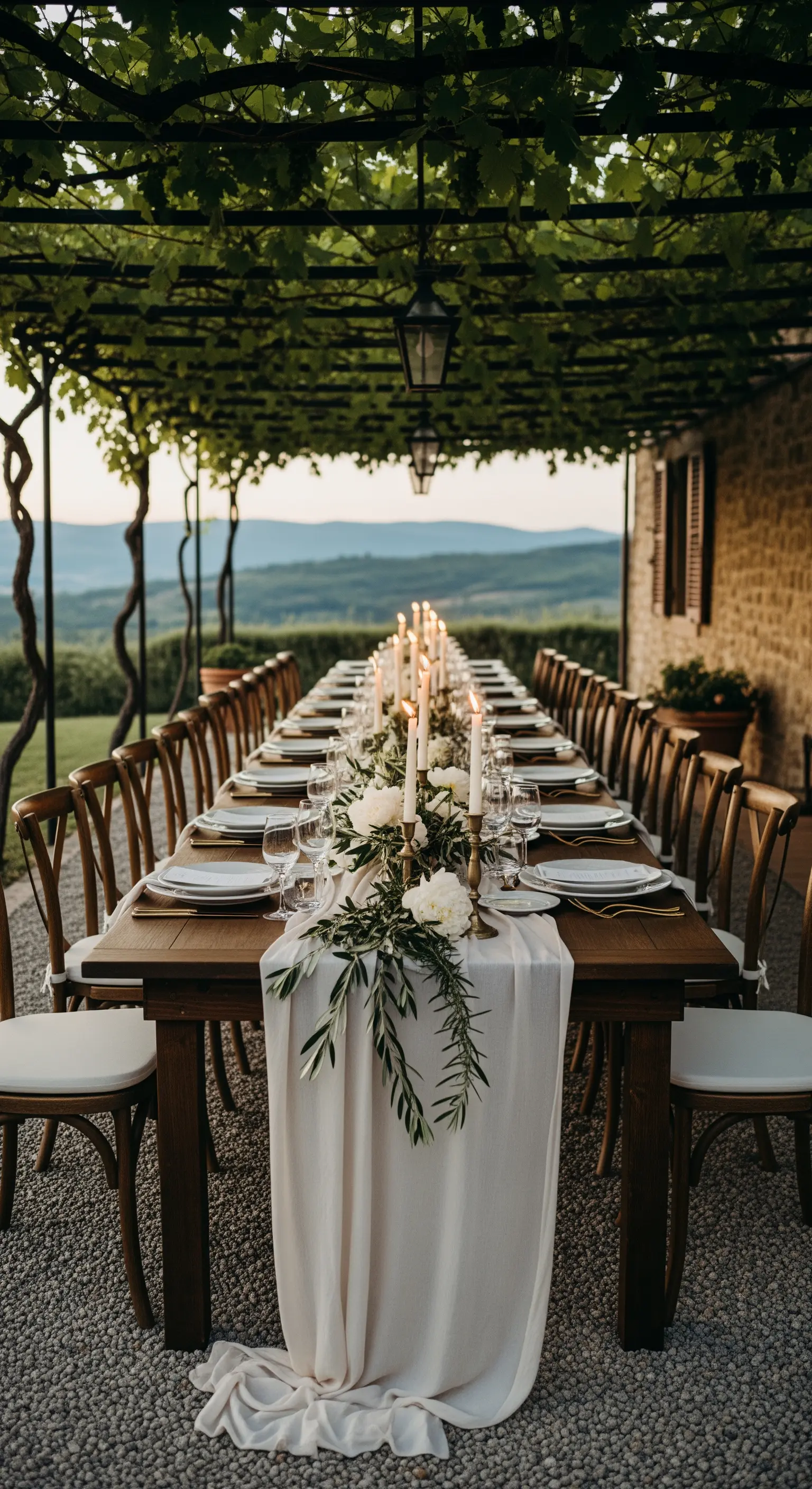 Lange Hochzeitstafel mit weißem Läufer, Kerzen und Olivenzweigen unter einer Wein-Pergola