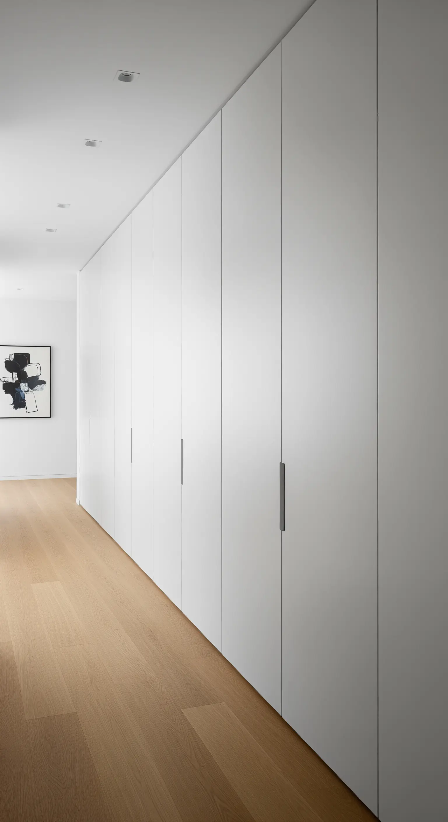 Langer Flur mit deckenhohen, grifflosen weißen Einbauschränken.