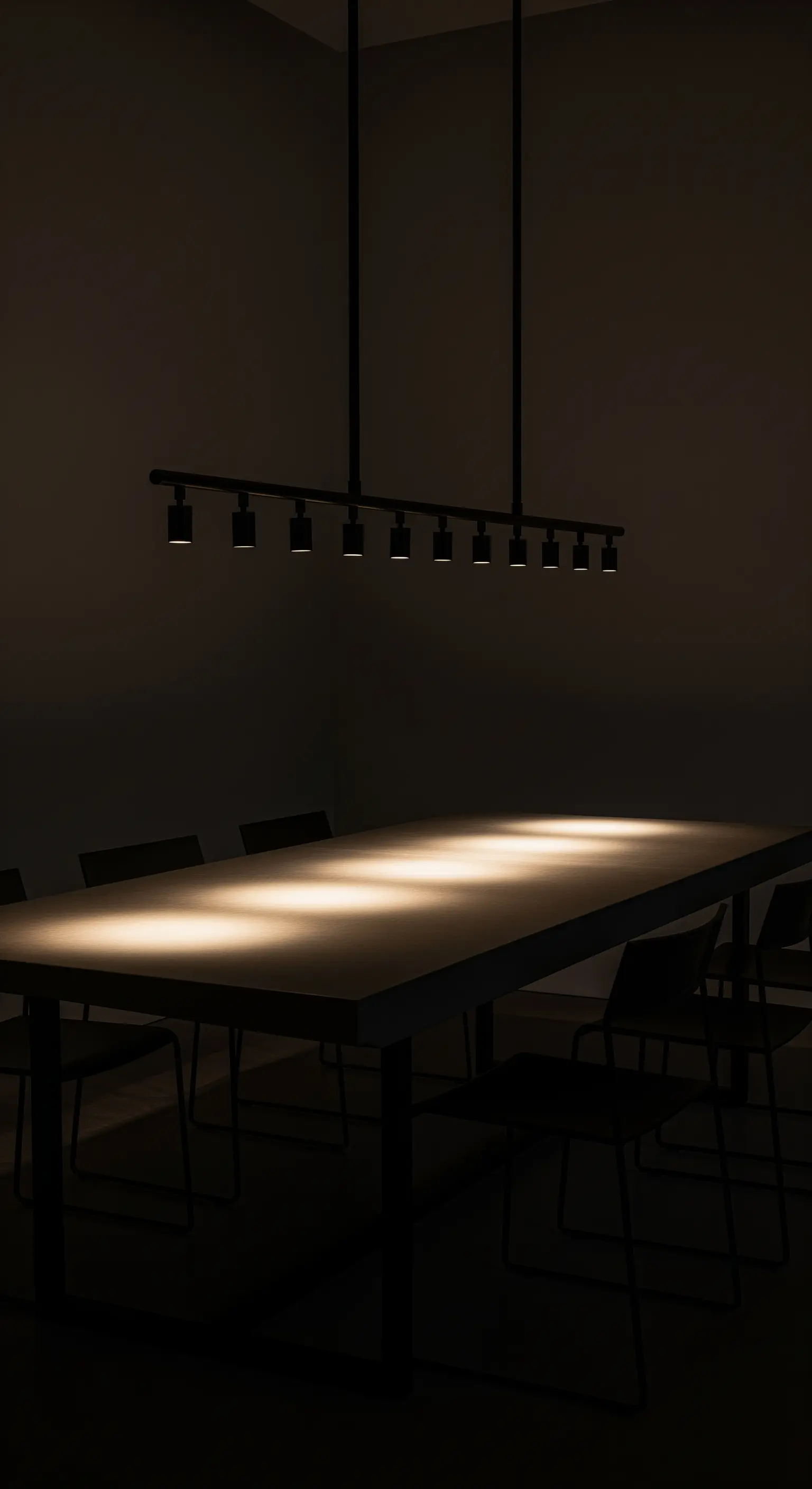 Schwarze Schienenleuchte mit Spots, die einen langen Esstisch in einem dunklen Raum beleuchten.