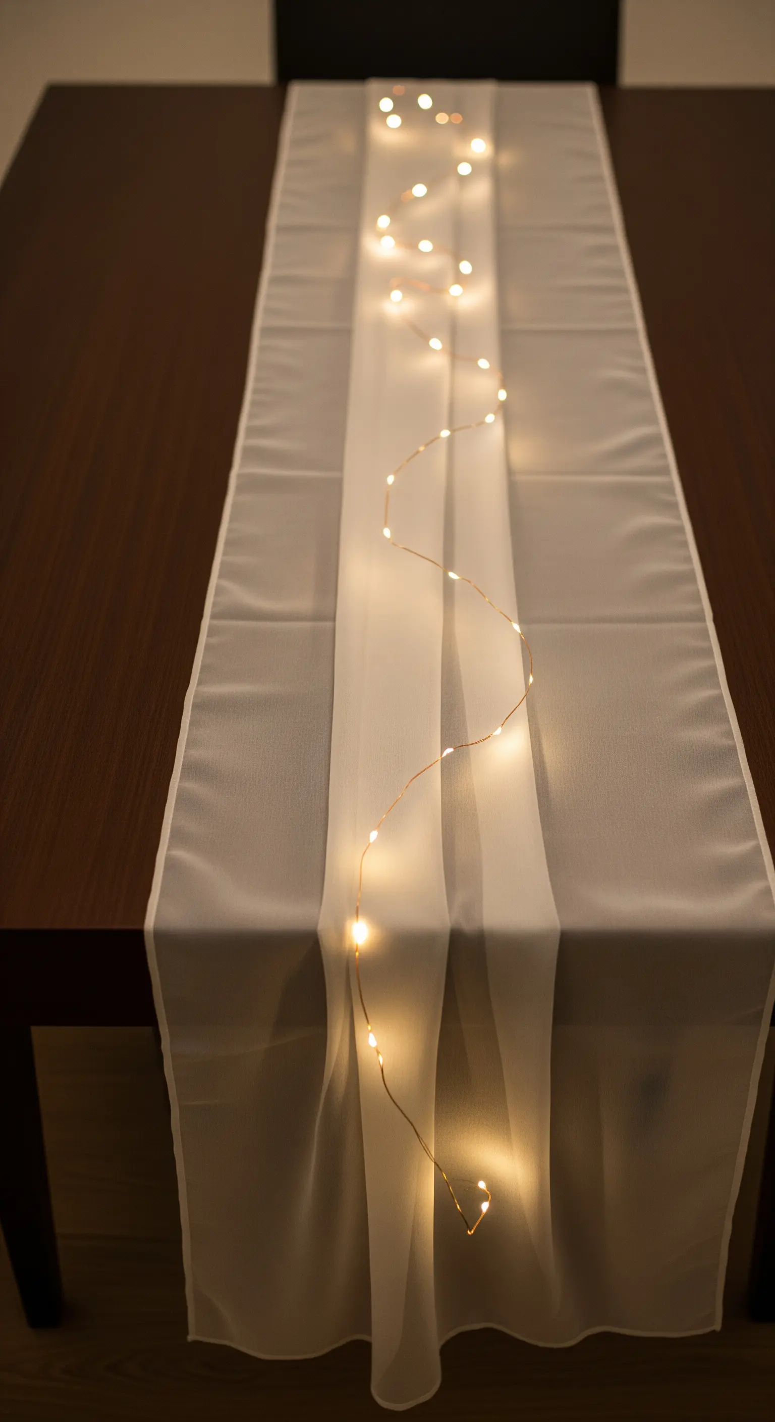 Minimalistischer Tischläufer aus weißem Stoff mit einer einzelnen, geschwungenen Lichterkette.