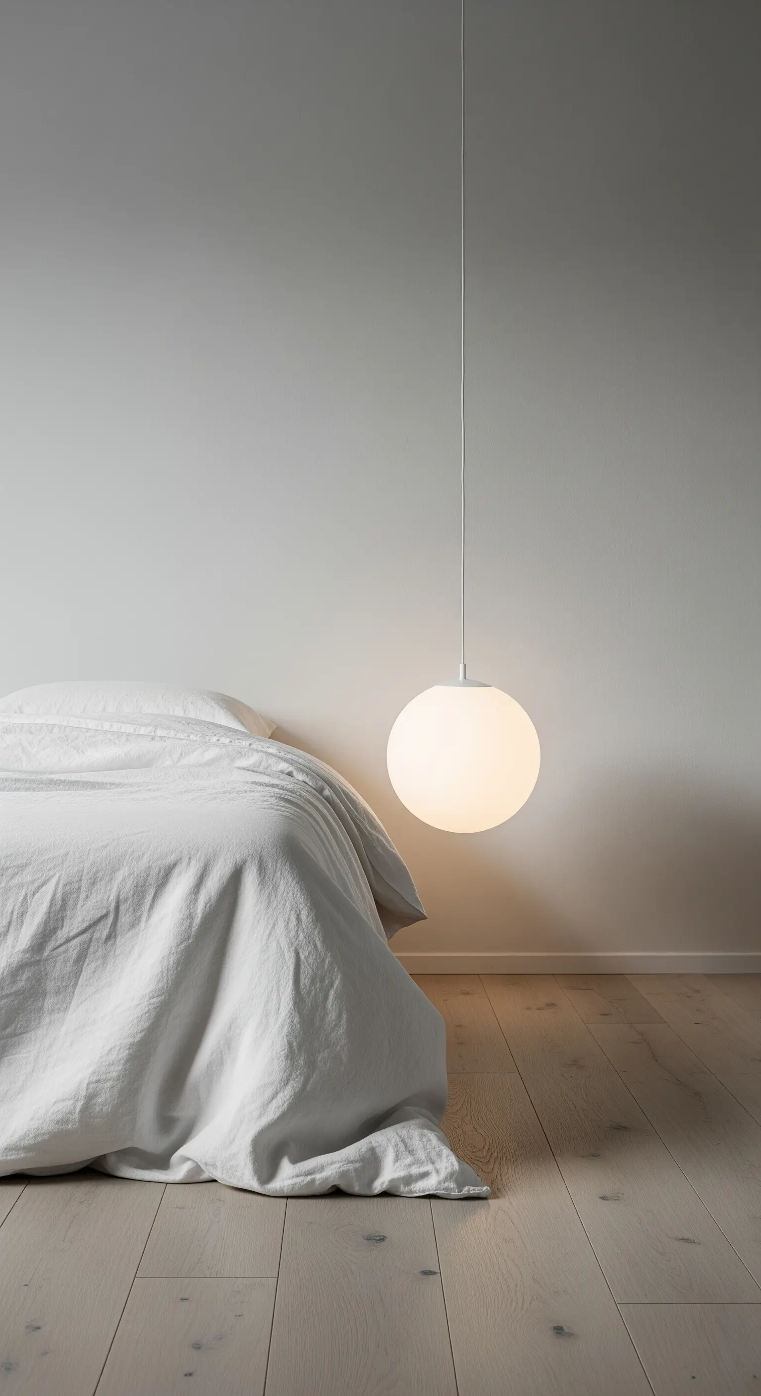 Einzelne, tief hängende Kugel-Pendelleuchte aus mattem Glas neben einem Bett.