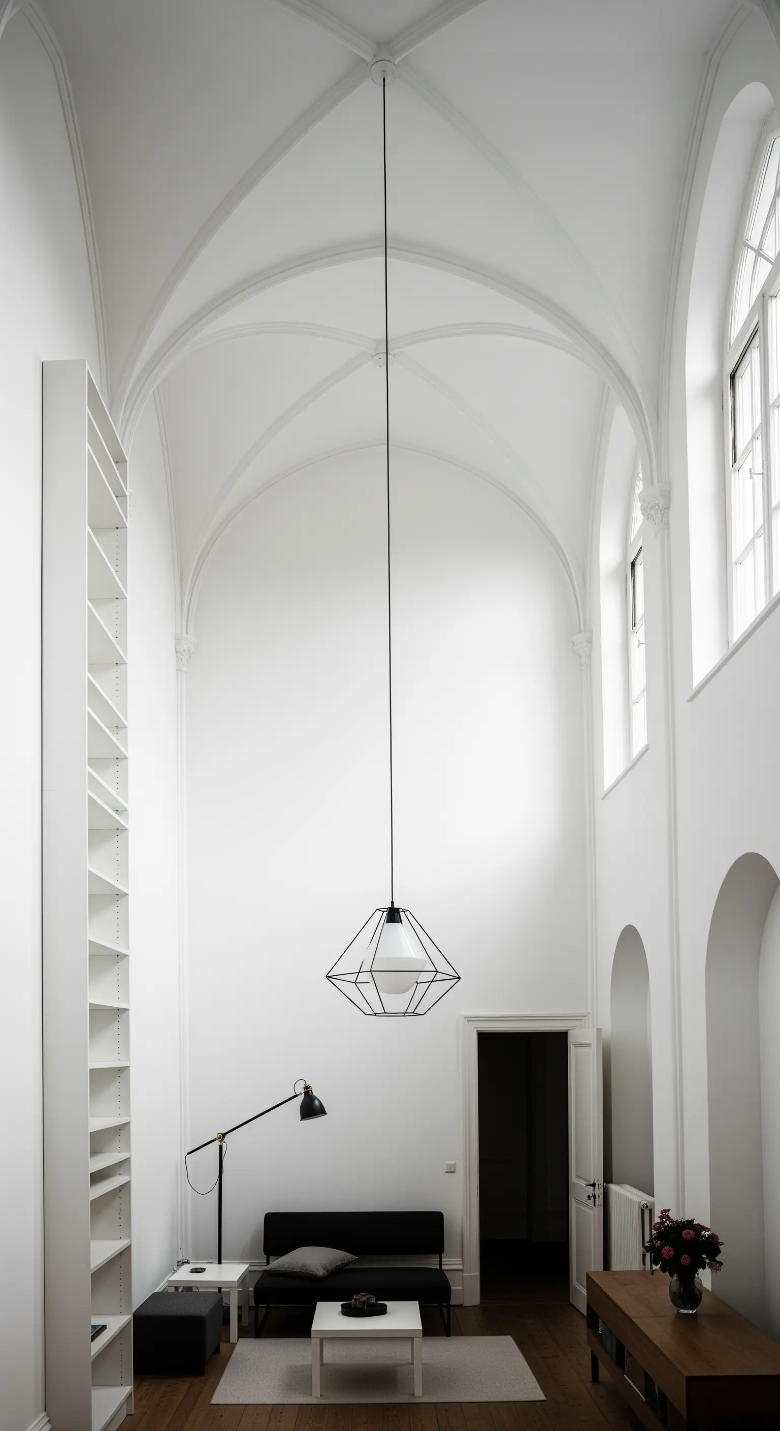 Hoher, weißer Raum mit Gewölbedecke, betont durch eine tief hängende, geometrische Lampe.
