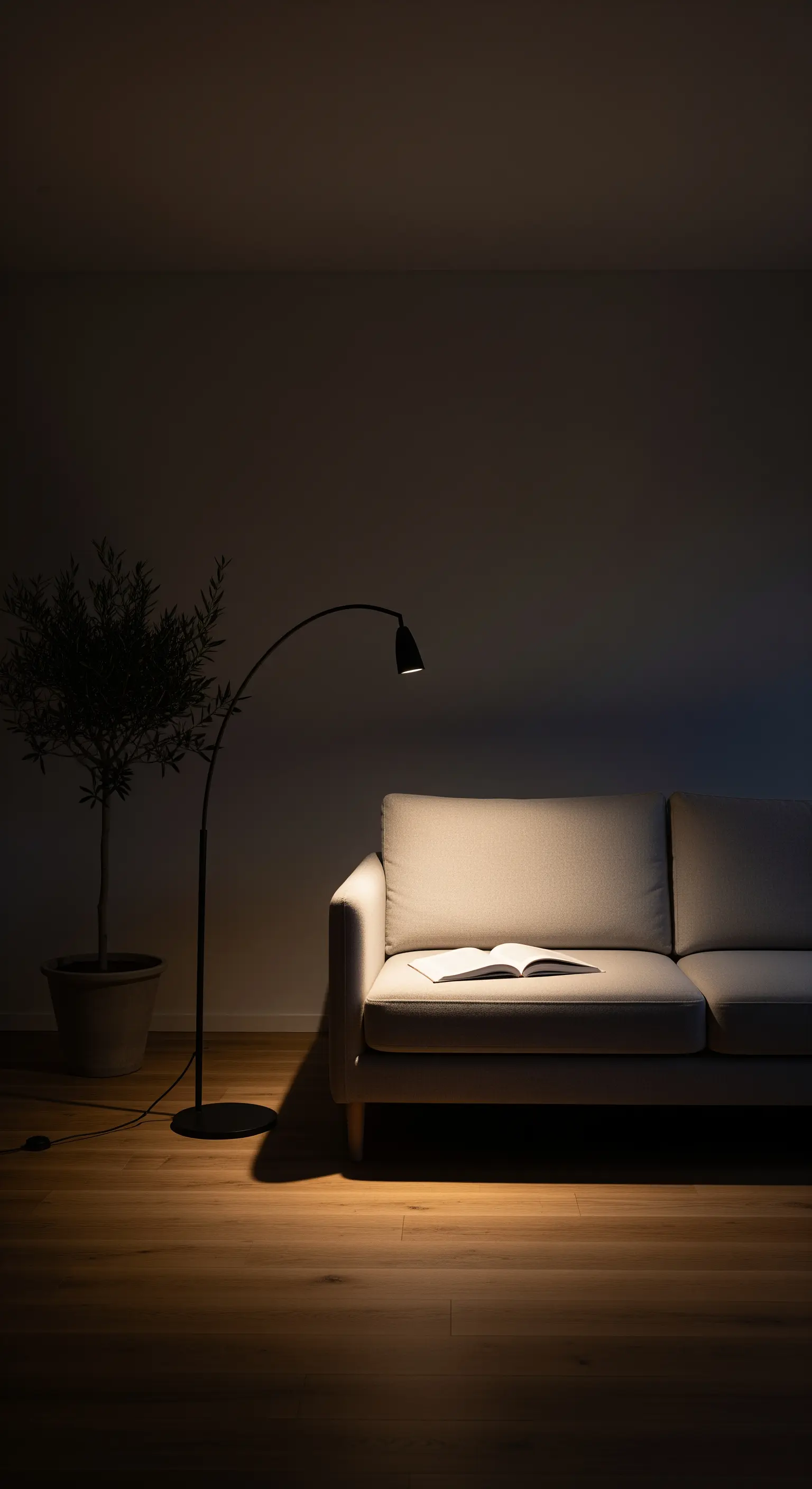 Minimalistische Bogenlampe beleuchtet ein beiges Sofa in einem dunklen Raum.