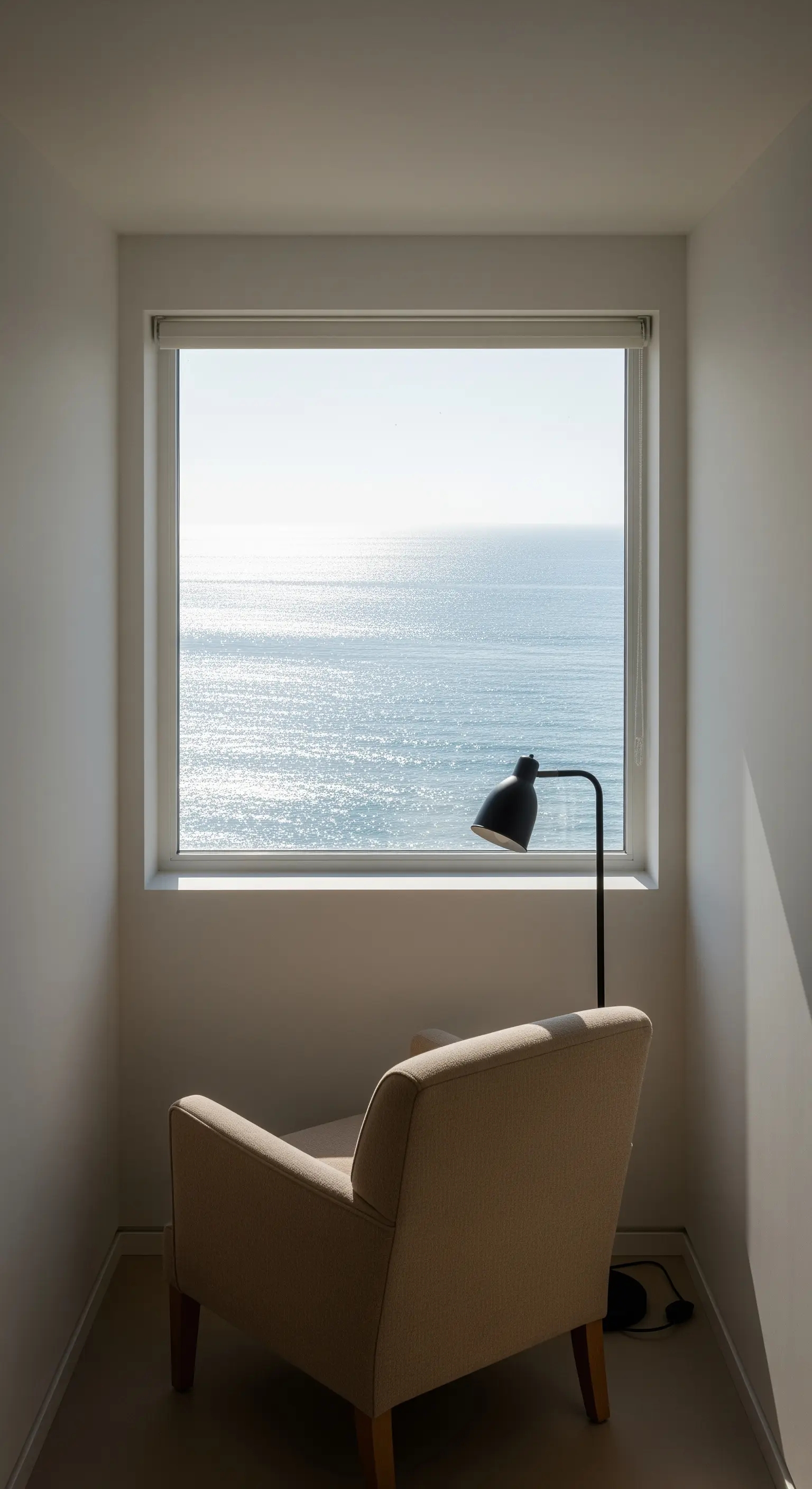 Ein beiger Sessel in einer kleinen Nische vor einem Fenster mit Meerblick.