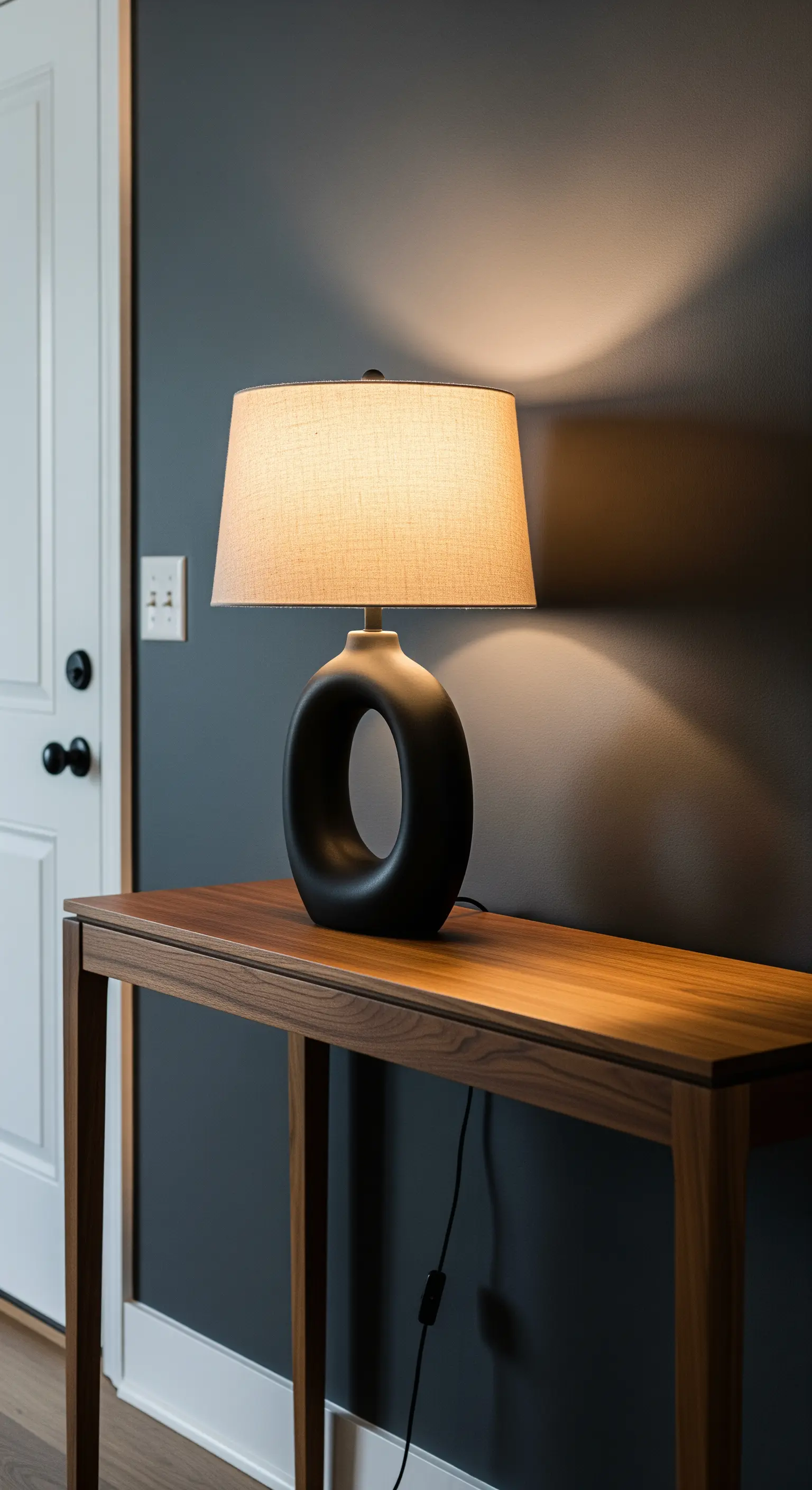 Eine skulpturale Tischlampe mit schwarzem Fuß steht auf einer Holzkonsole im Eingangsbereich.