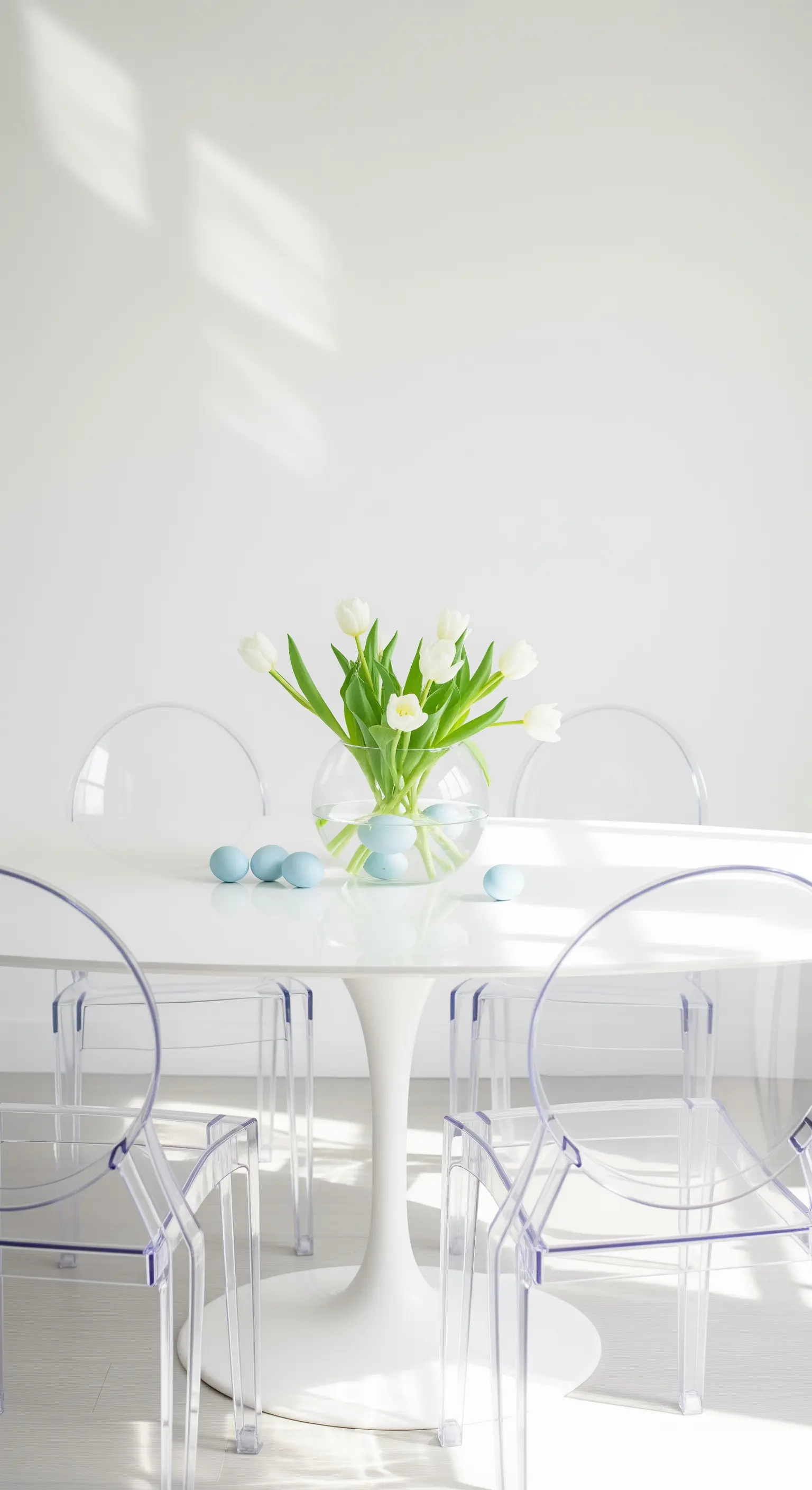 Weiße Tulpen und hellblaue Eier auf einem weißen Esstisch mit transparenten Stühlen