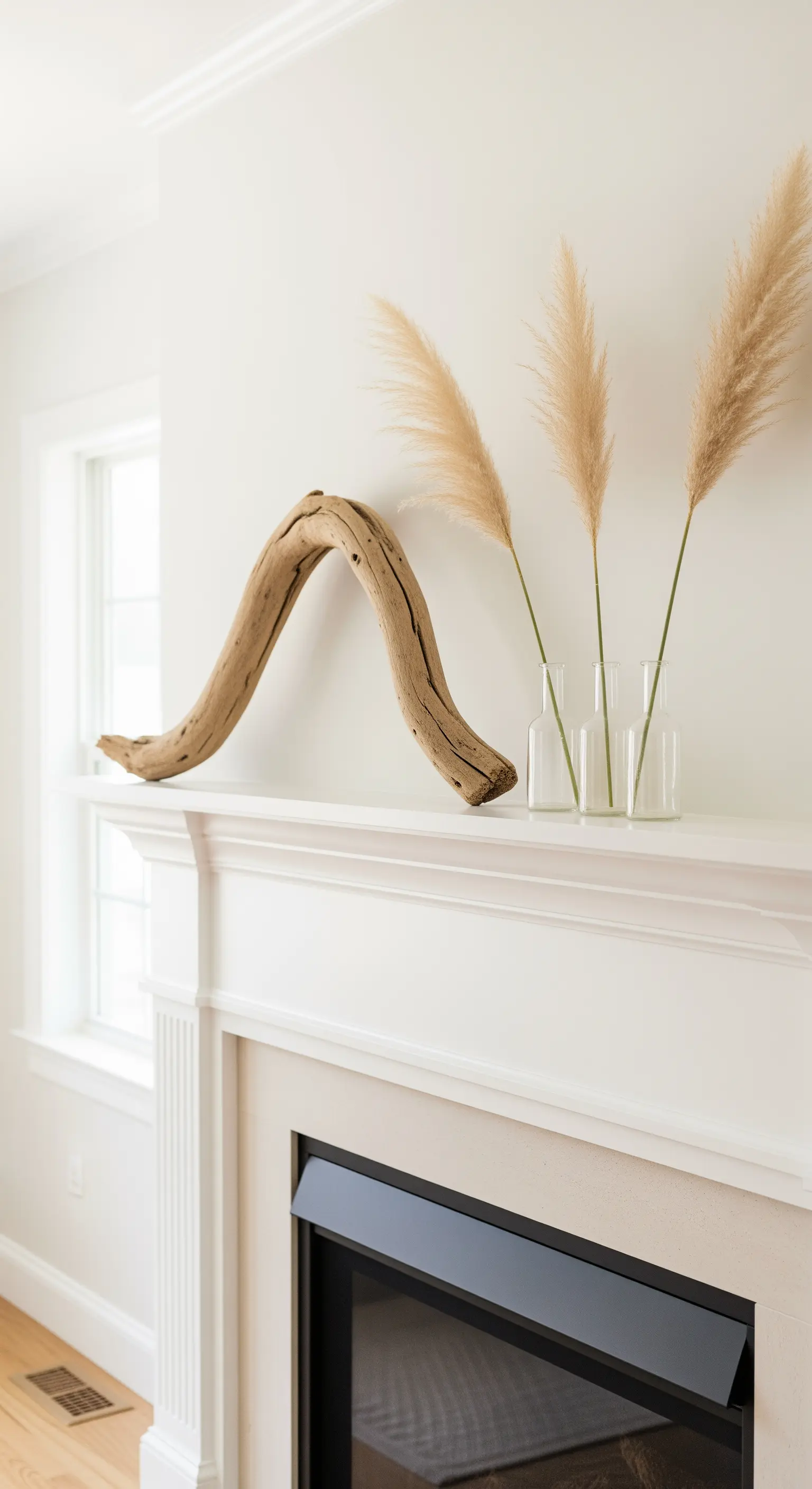Kaminumrandung mit skulpturalem Treibholz und Pampasgras in Glasvasen.