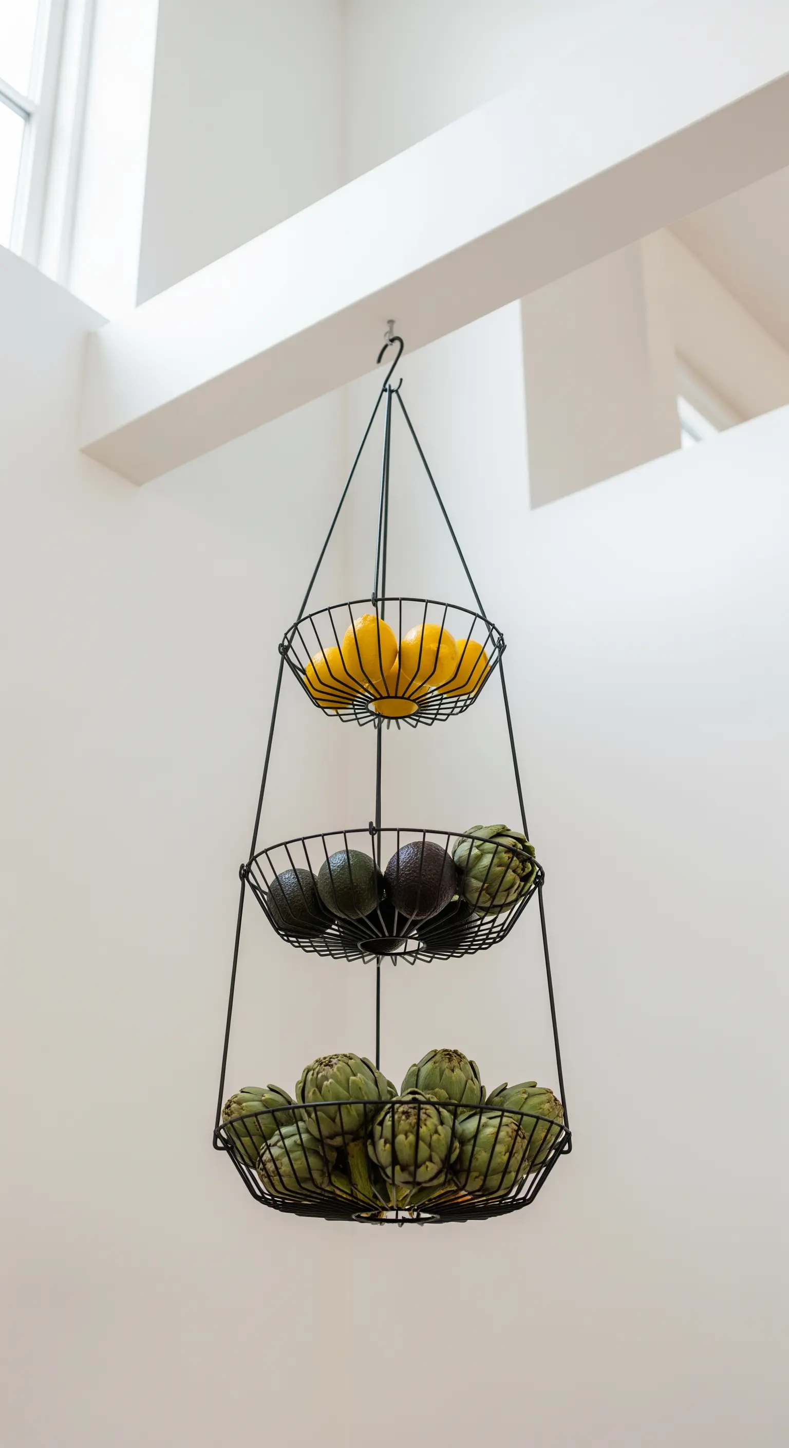 Schwarze, dreistöckige Hänge-Etagere aus Draht, gefüllt mit Zitronen, Avocados und Artischocken.
