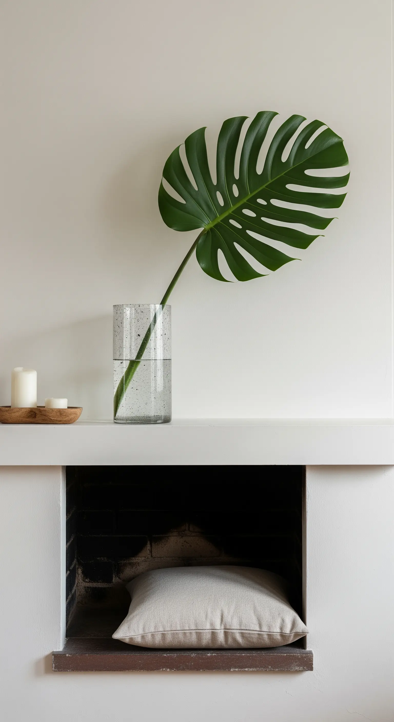 Ein einzelnes, großes Monstera-Blatt in einer hohen Glasvase auf einem minimalistischen weißen Kaminsims