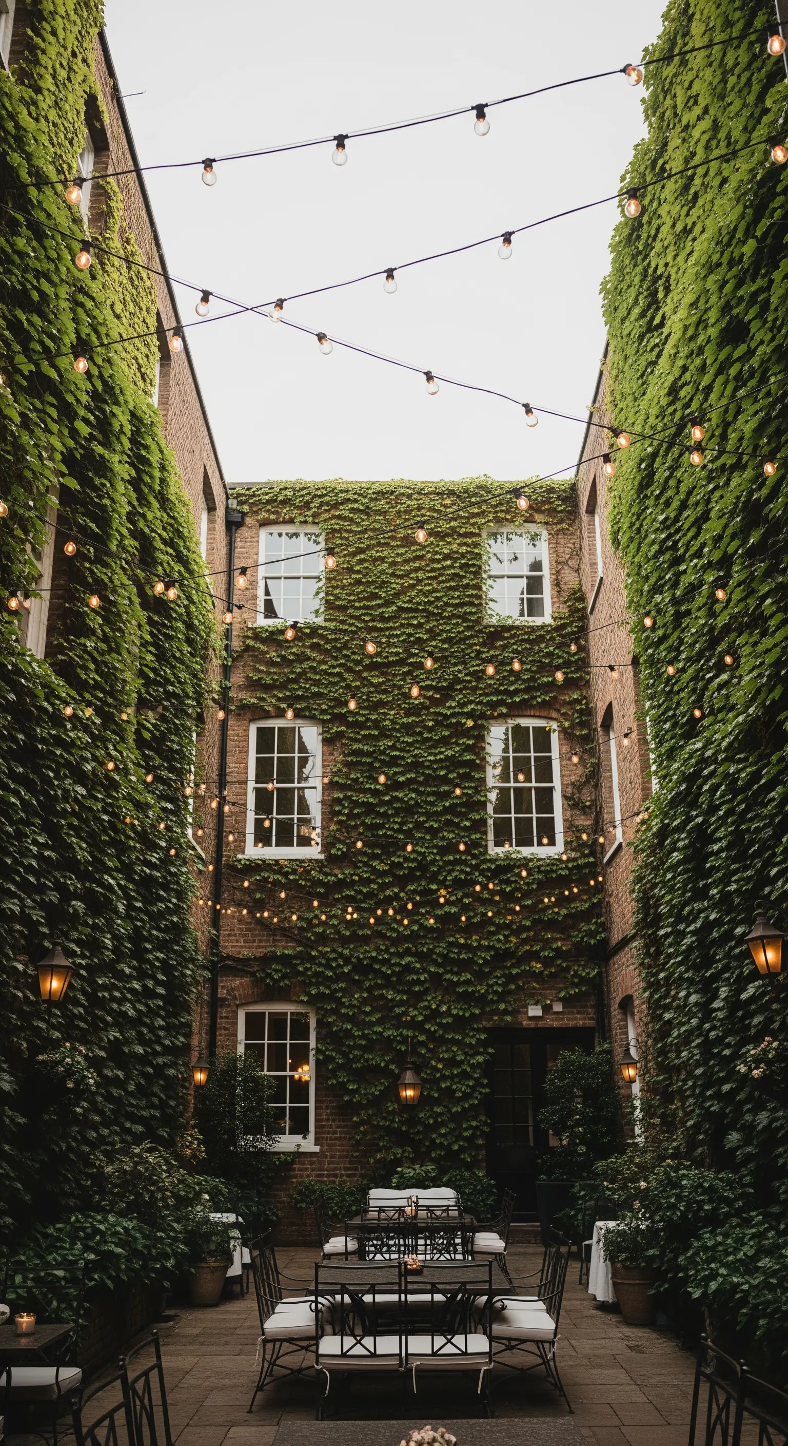 Lichterketten sind zwischen efeubewachsenen Backsteinmauern in einem schmalen Innenhof gespannt.
