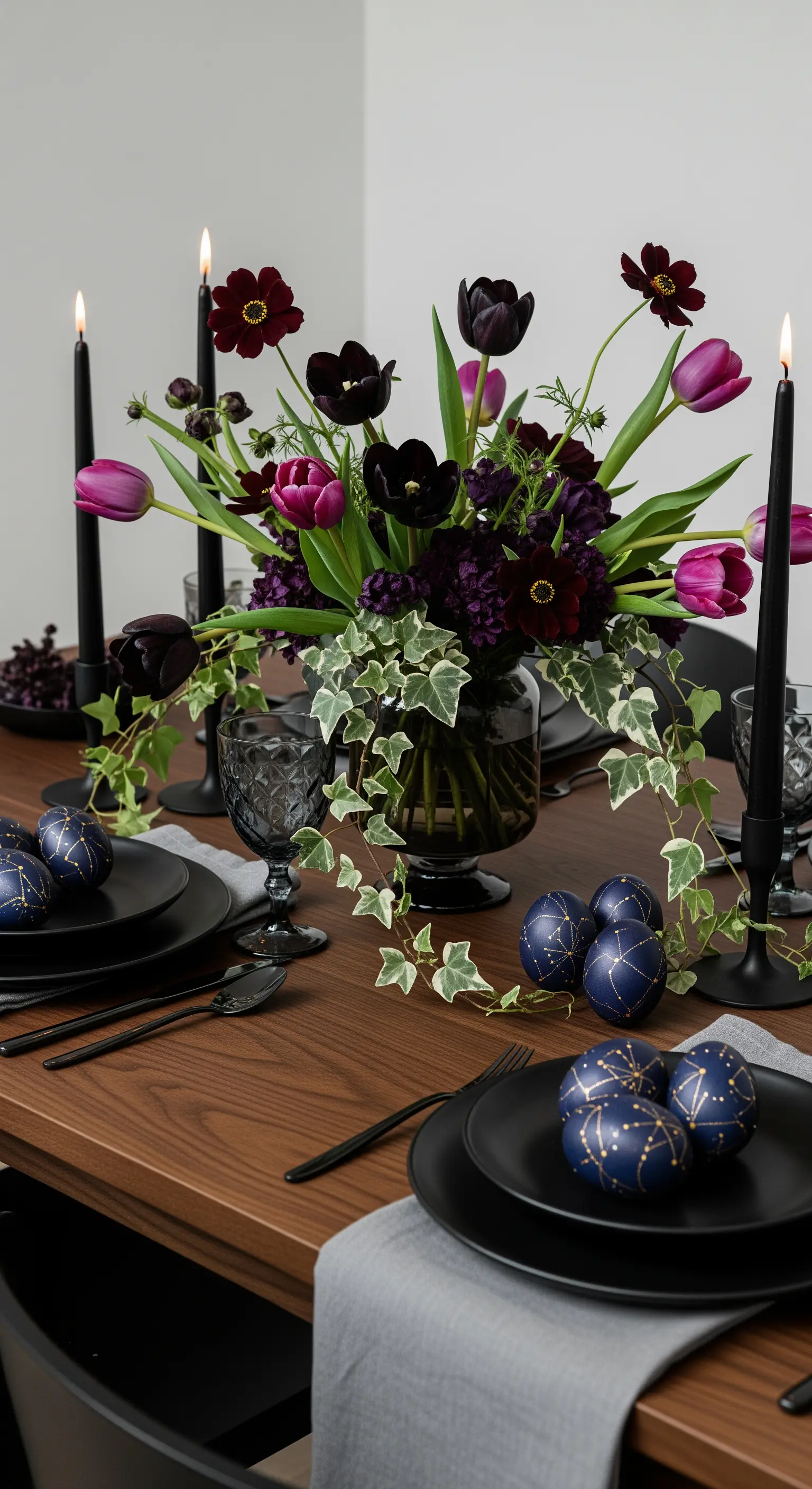 Dunkle, dramatische Ostertafel mit schwarzen Tellern, Kerzen und lila Blumen.