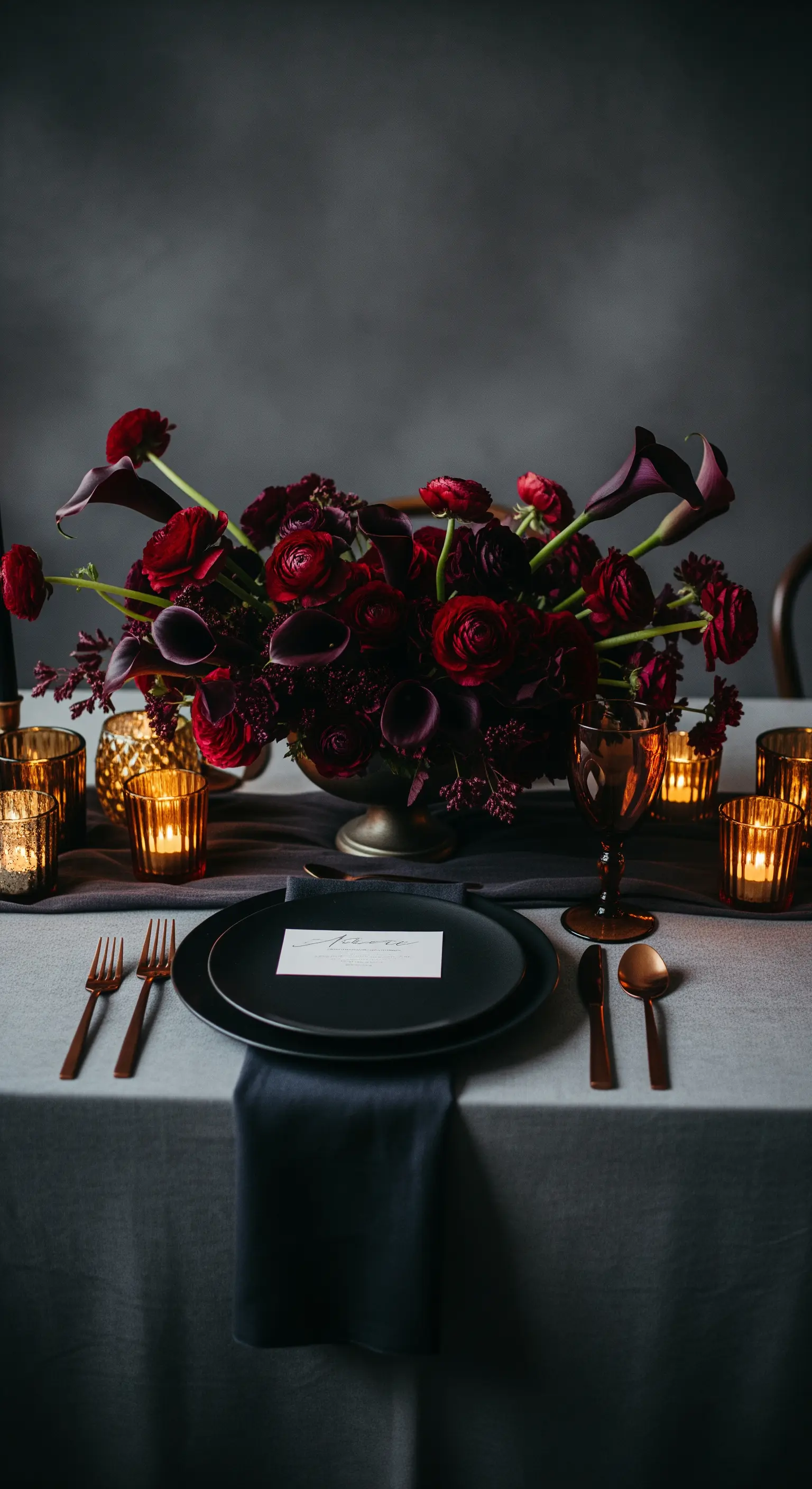 Dramatische Tischdekoration mit dunklen Blumen, schwarzem Geschirr und bronzenen Kerzenhaltern