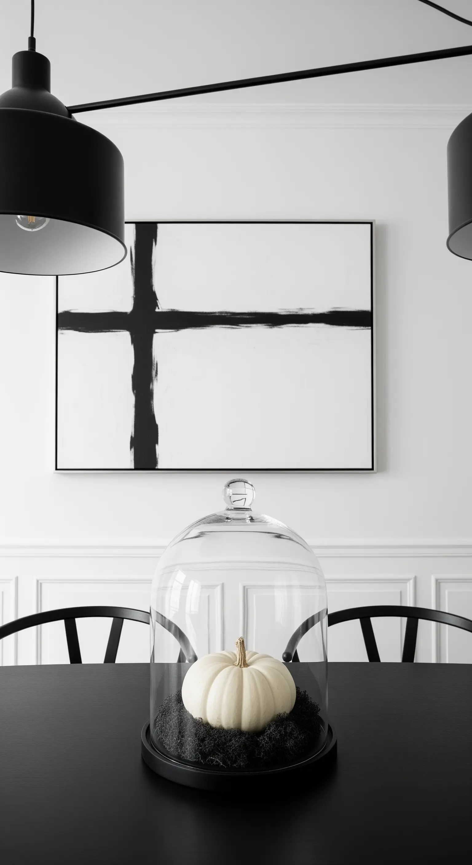 Esstisch mit weißem Kürbis unter Glasglocke, schwarzem Moos und minimalistischer Kunst.