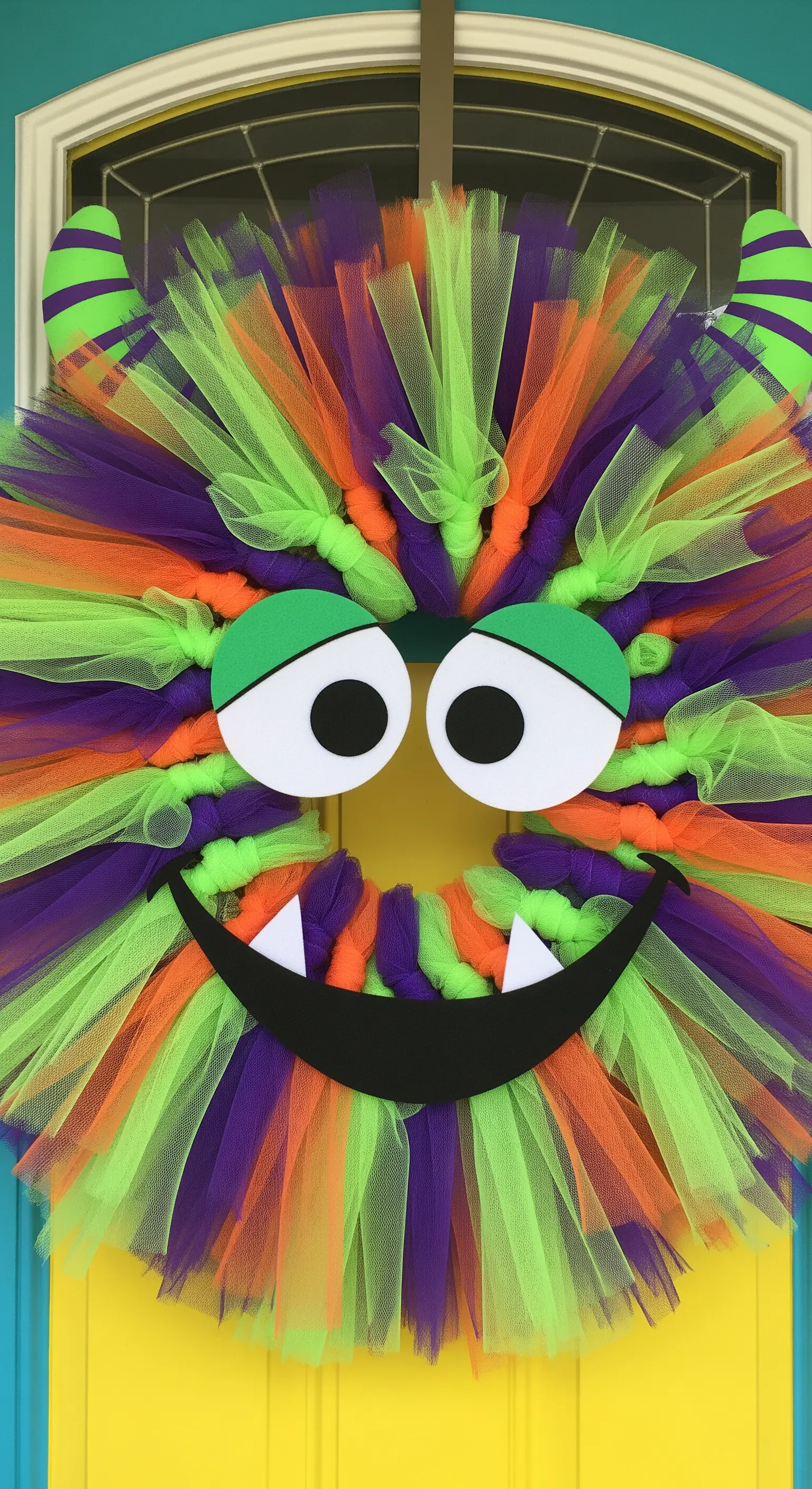 Ein bunter Türkranz aus Tüll in Grün, Orange und Lila, gestaltet wie ein freundliches Monstergesicht.