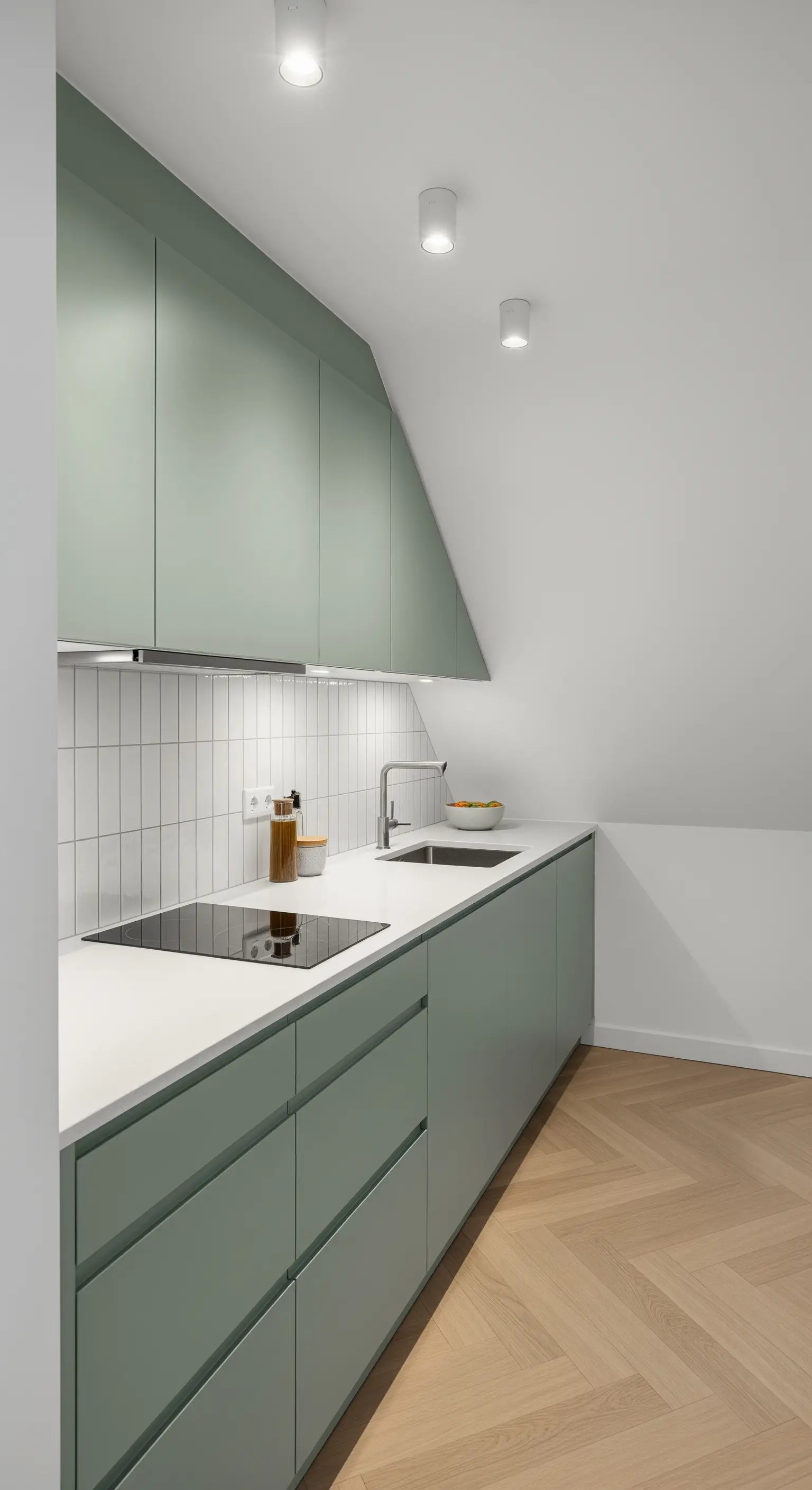 Moderne Küche mit salbeigrünen, grifflosen Schränken und vertikalen weißen Fliesen unter einer Dachschräge.