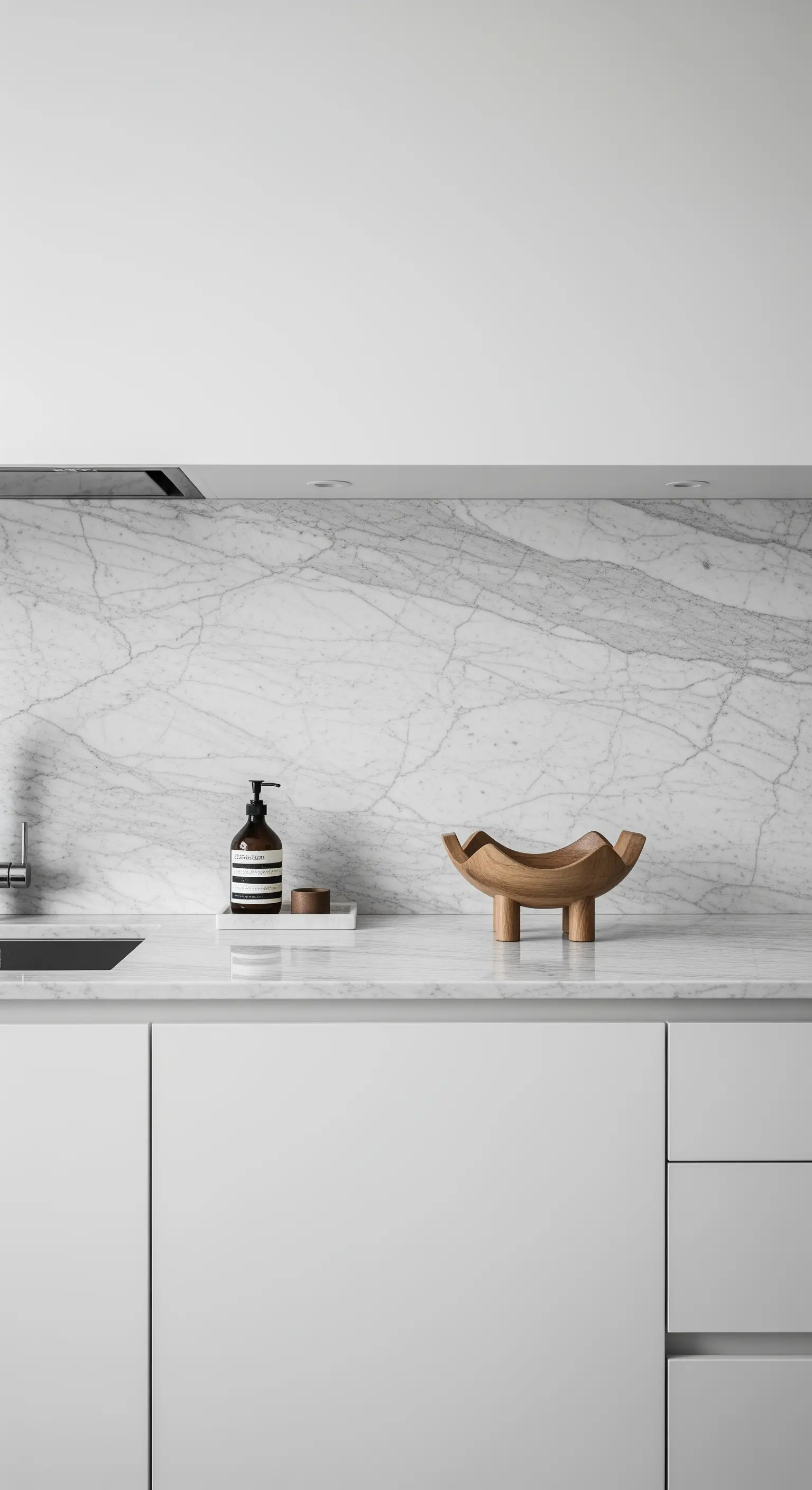 Minimalistische weiße Küche mit Marmorrückwand und einer einzelnen skulpturalen Holzschale als Deko.