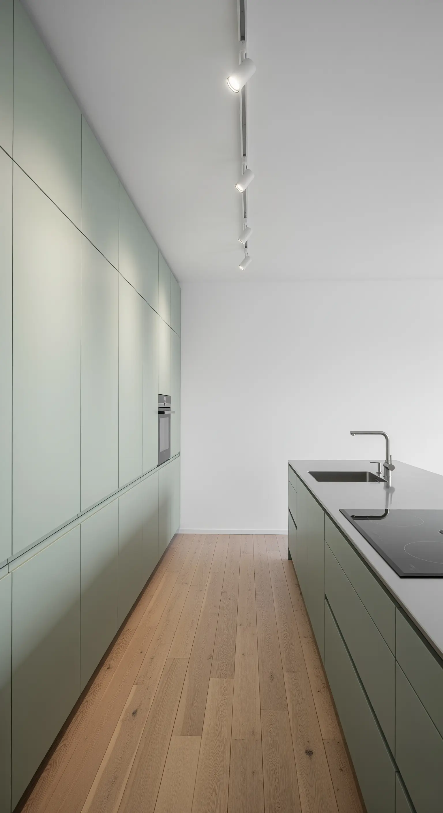 Lange, minimalistische Küche mit deckenhohen, salbeigrünen Schränken ohne Griffe.