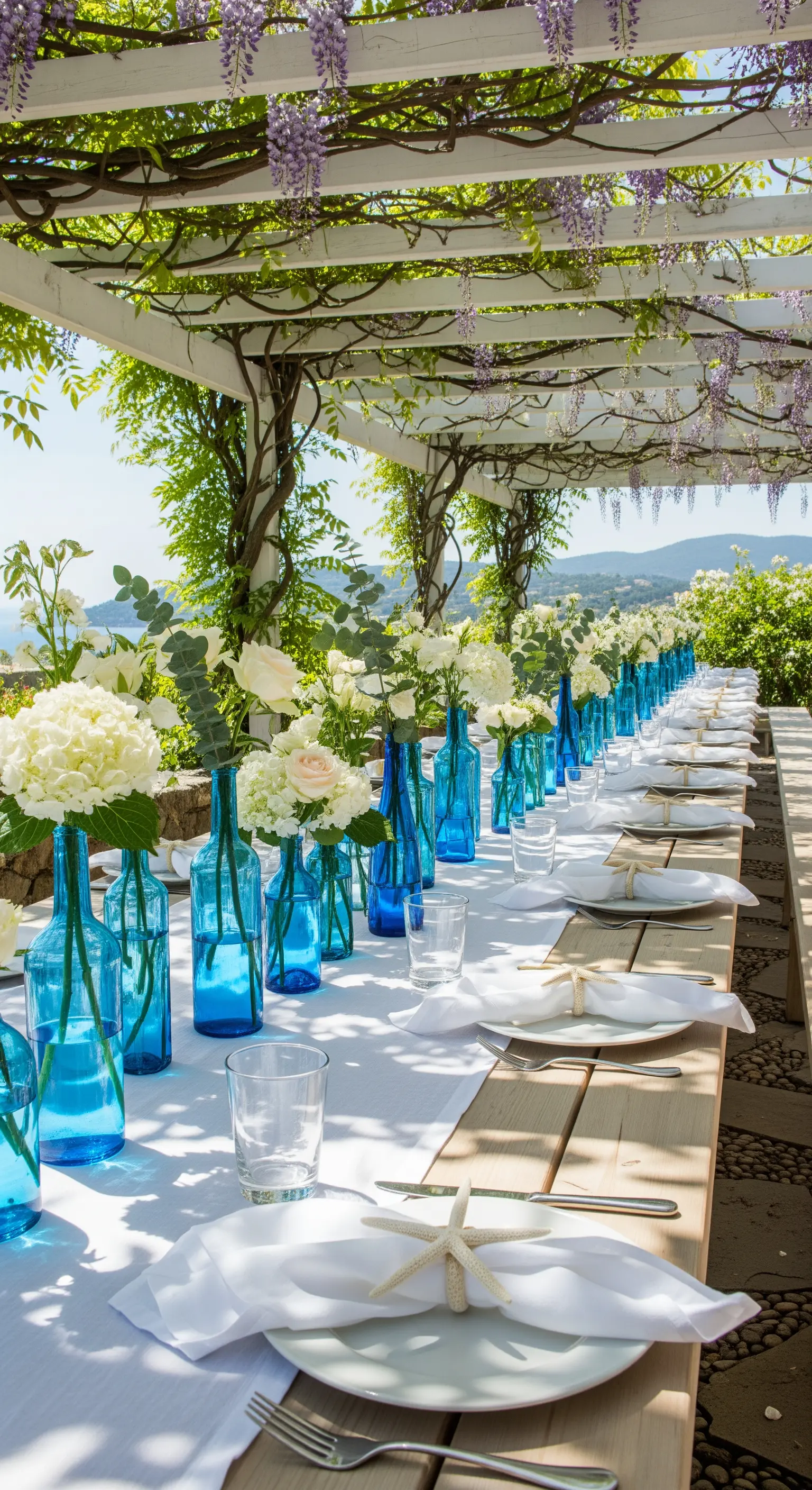 Outdoor-Tafel unter Pergola mit blauen Flaschenvasen, weißen Blumen, Seestern-Deko