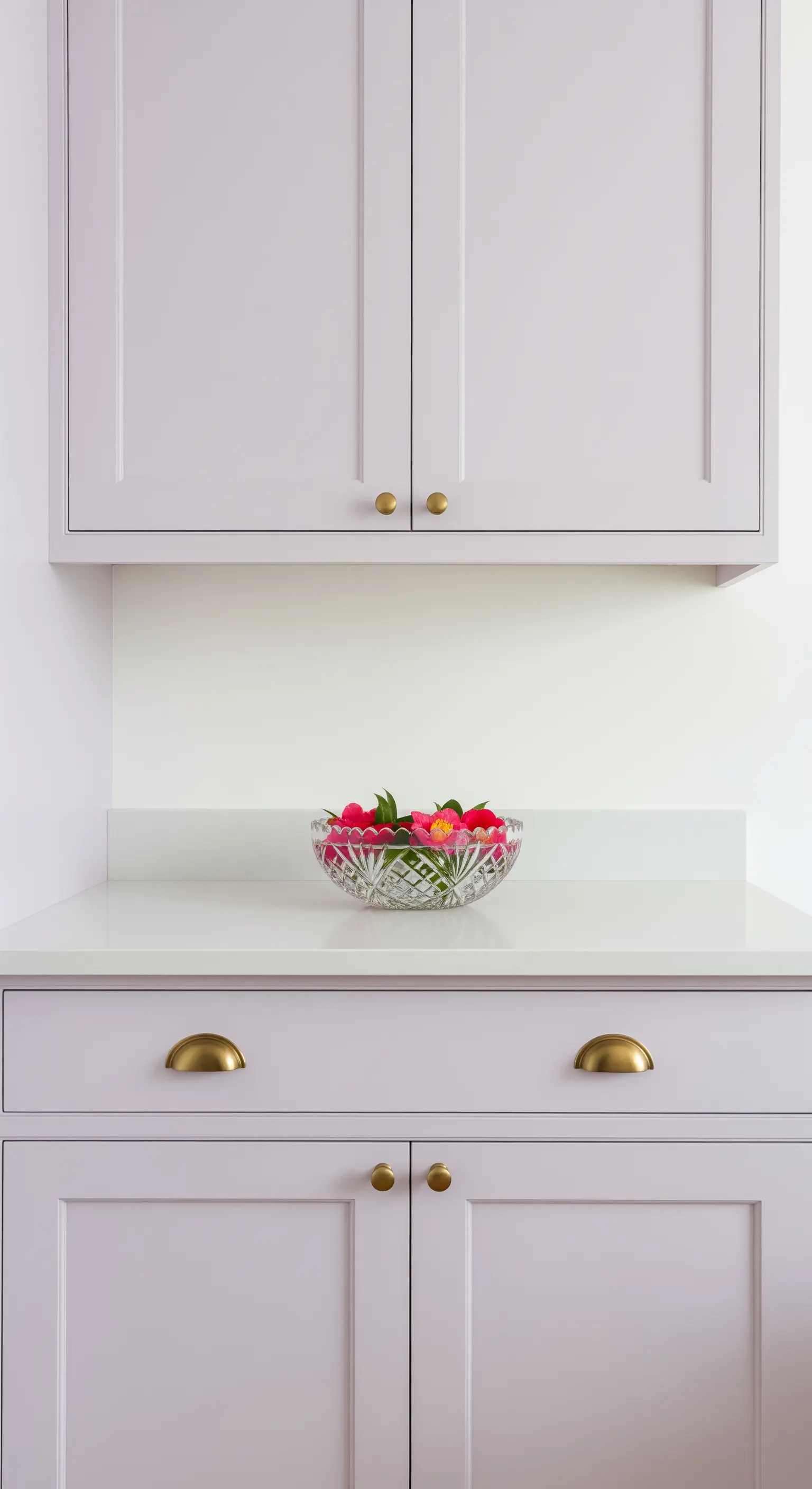 Fliederfarbene Küchenschränke mit eleganten goldenen Griffen und einer Kristallschale mit Blüten