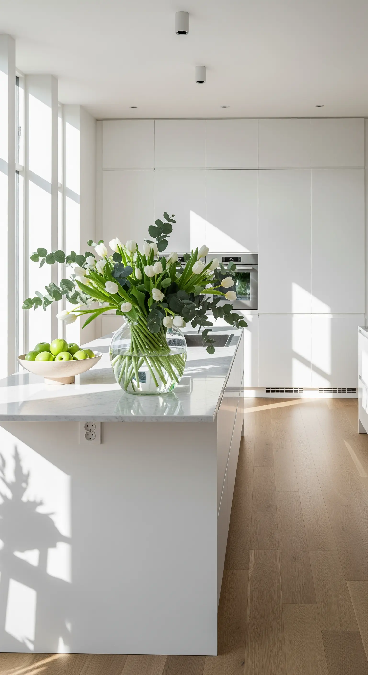 Weiße Tulpen und Eukalyptus in Glasvase auf minimalistischer Kücheninsel