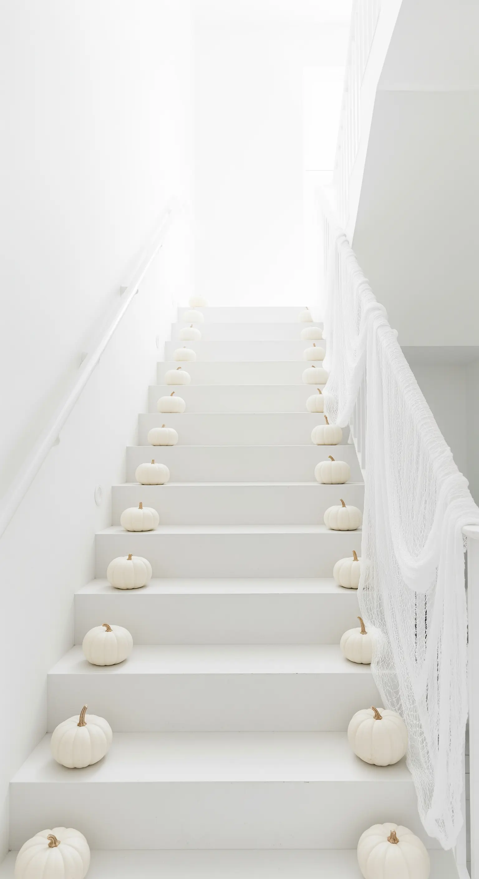 Weiße Treppe mit einer Reihe von weißen Kürbissen und weißem Schleier am Geländer