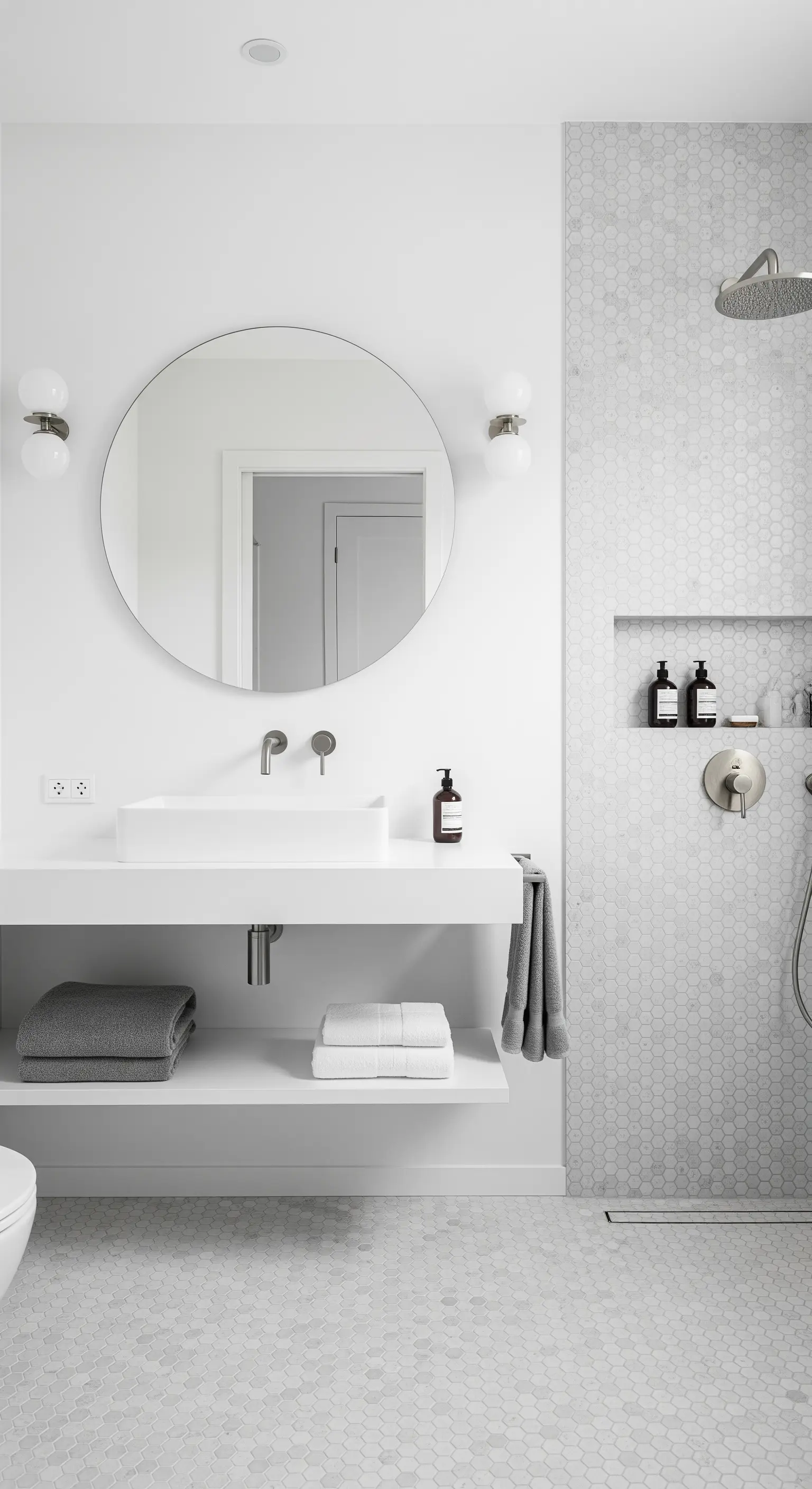 Weißes Bad mit hexagonalen Mosaikfliesen, rundem Spiegel und schwebendem Waschtisch.