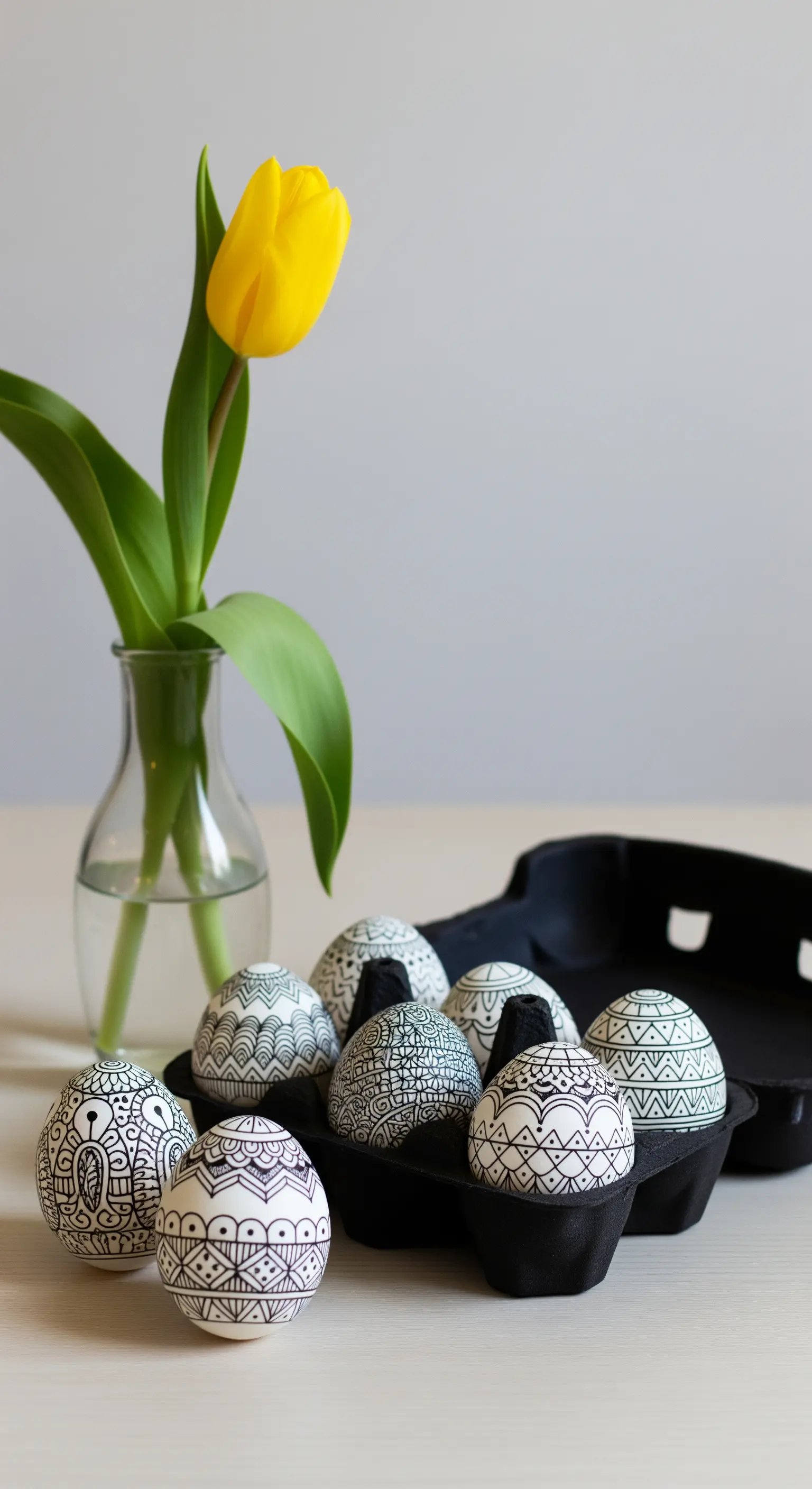 Schwarzer Eierkarton mit schwarz-weiß gemusterten Eiern und gelber Tulpe