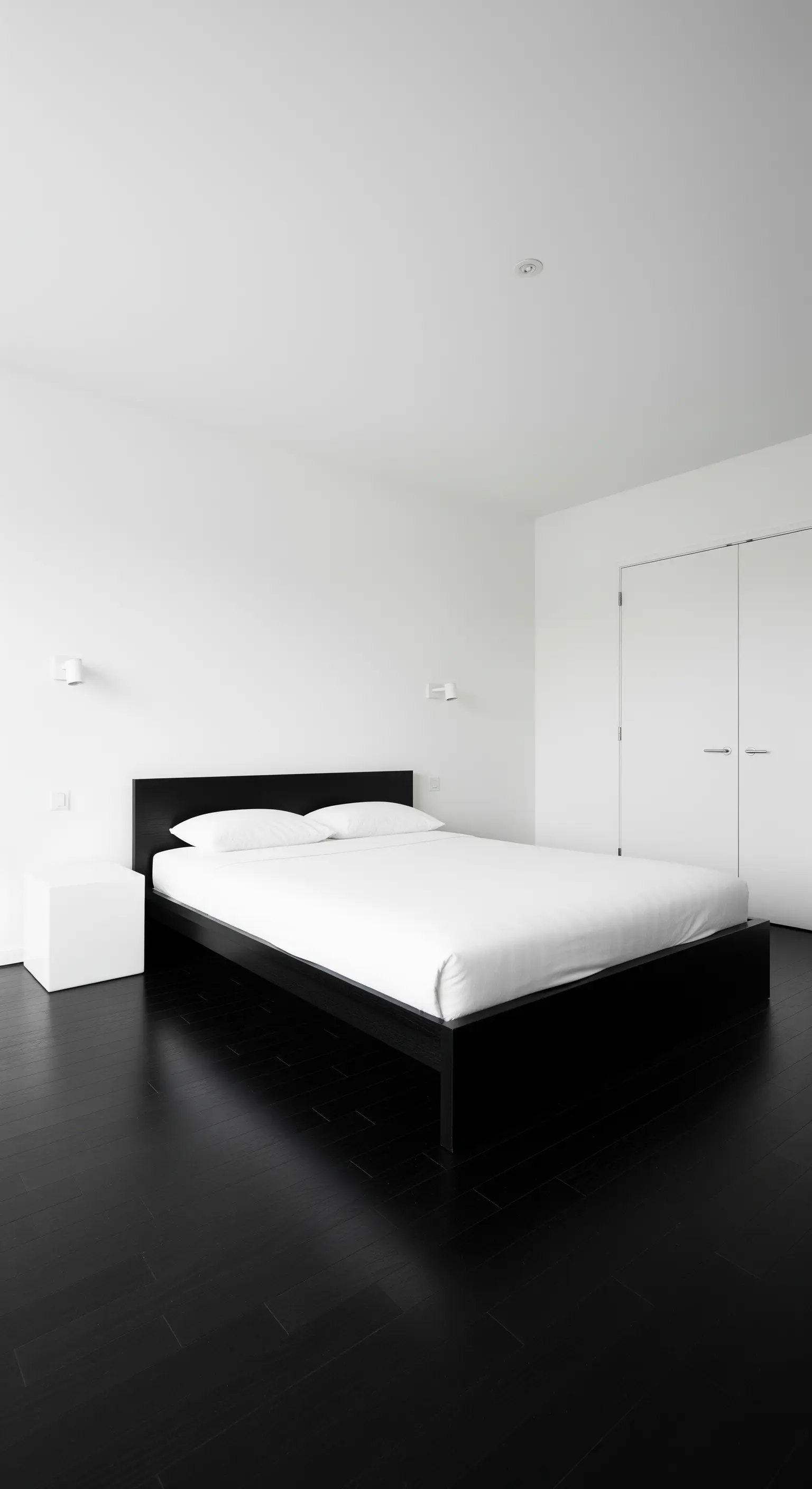 Minimalistisches Schlafzimmer mit weißen Wänden, schwarzem Boden und schwarzem Bett.
