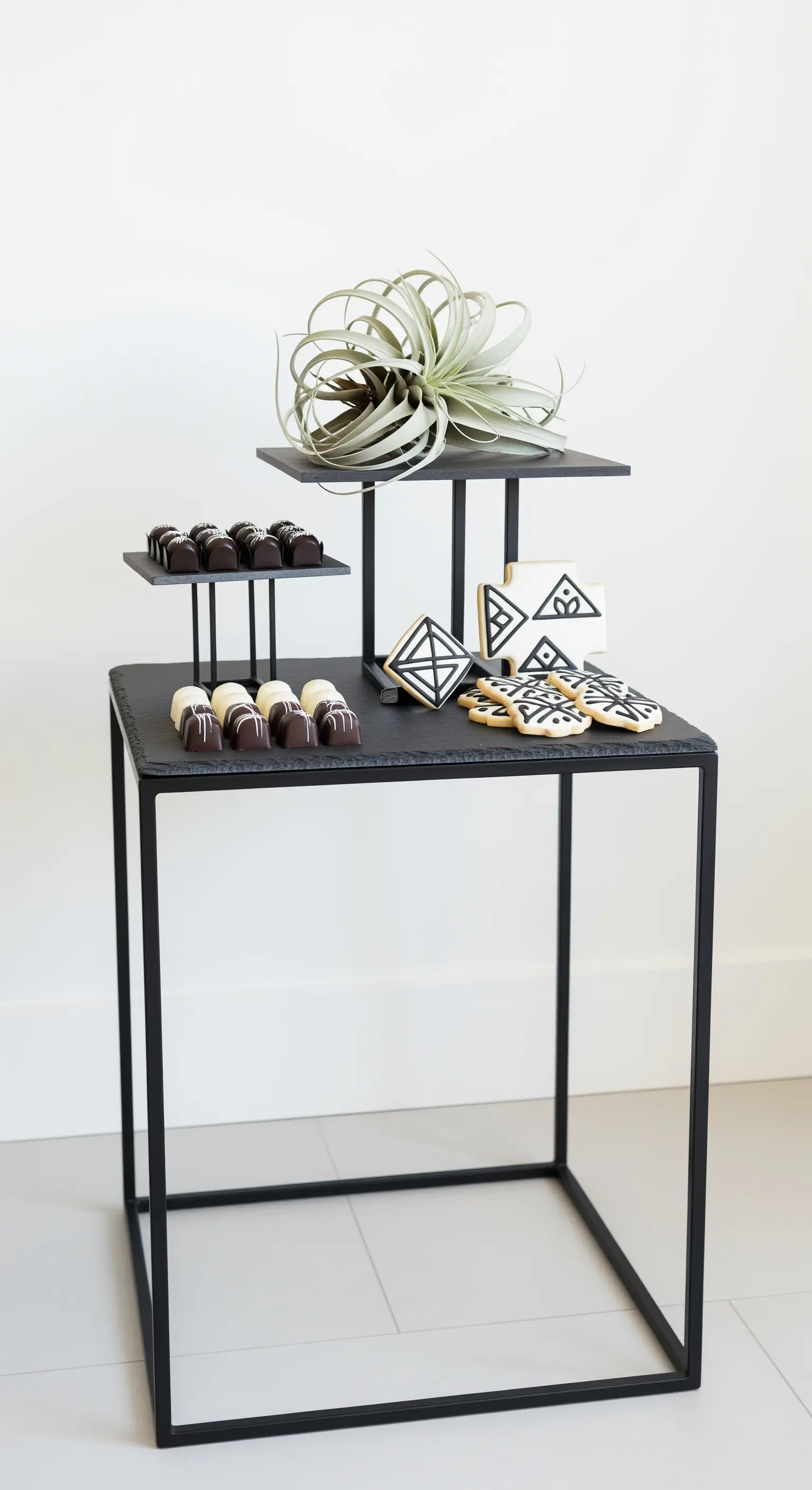 Moderne, schwarze Etagere mit grafisch verzierten Keksen und einer Luftpflanze.