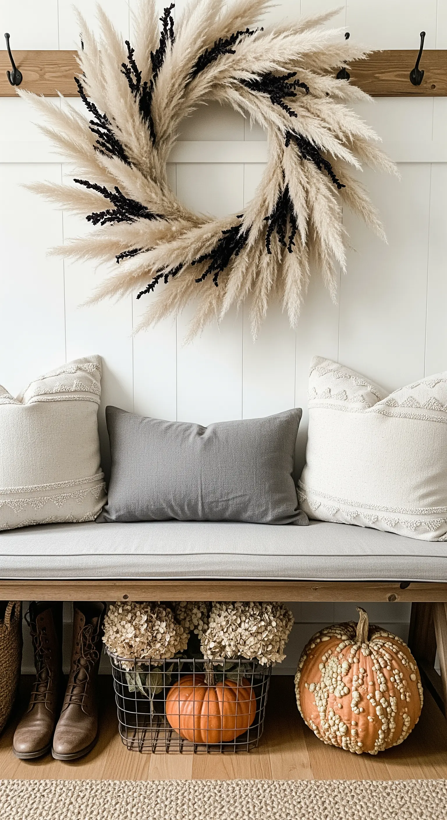 Pampasgras-Kranz mit schwarzen Akzenten über einer Holzbank mit Kissen.